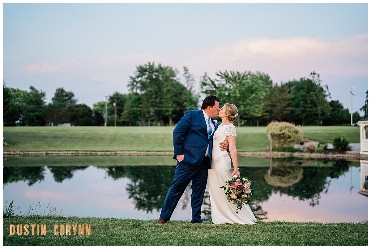 bride and groom kissing next to a lake after golden hour for their Spring Fort Wayne wedding