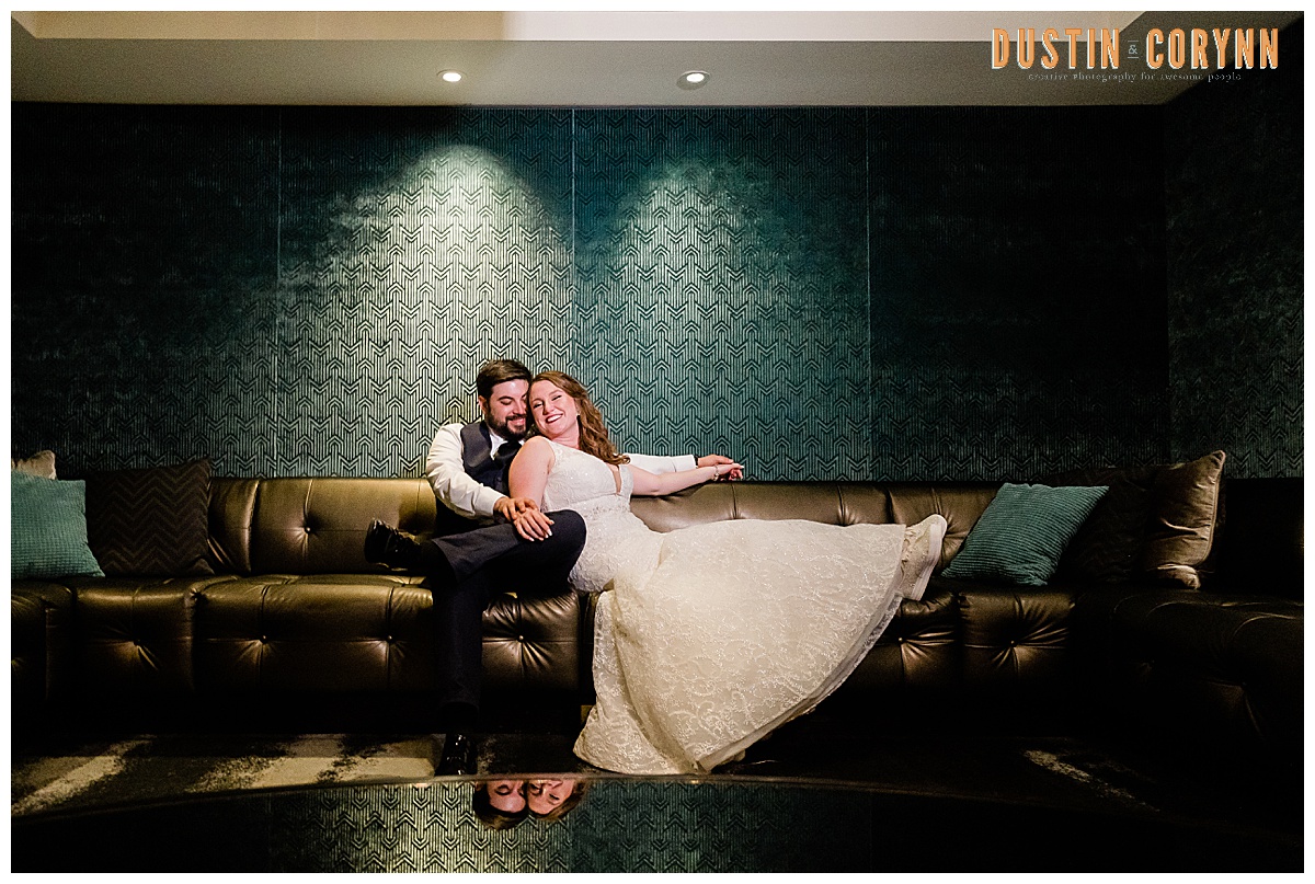 bride and groom sitting on a couch together for their Fort Wayne wedding day as the bride leans into the groom and they both smile take by Fort Wayne wedding photographers