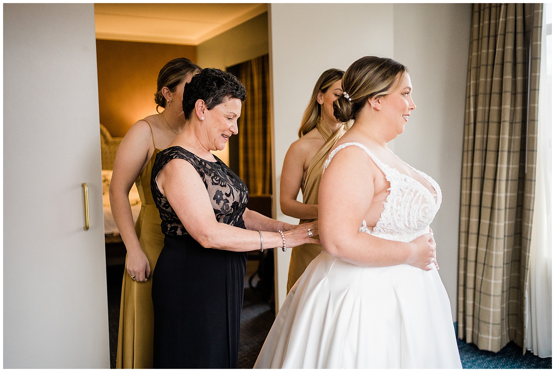 bride getting into dress with help of mother and bridesmaids on wedding day