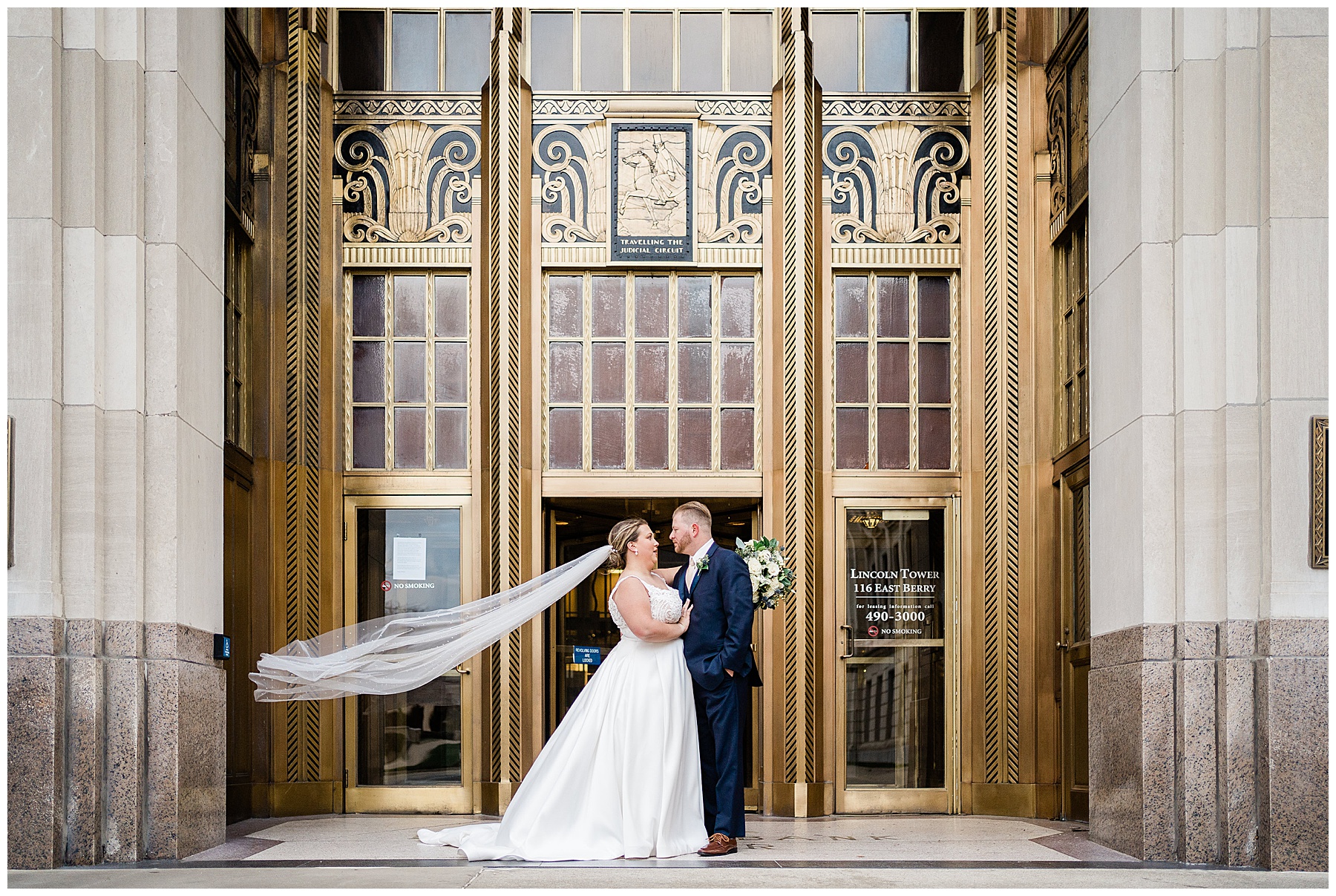 Fort Wayne wedding photography with bride and groom embracing outside of their wedding venue as the brides veil slows in the wind
