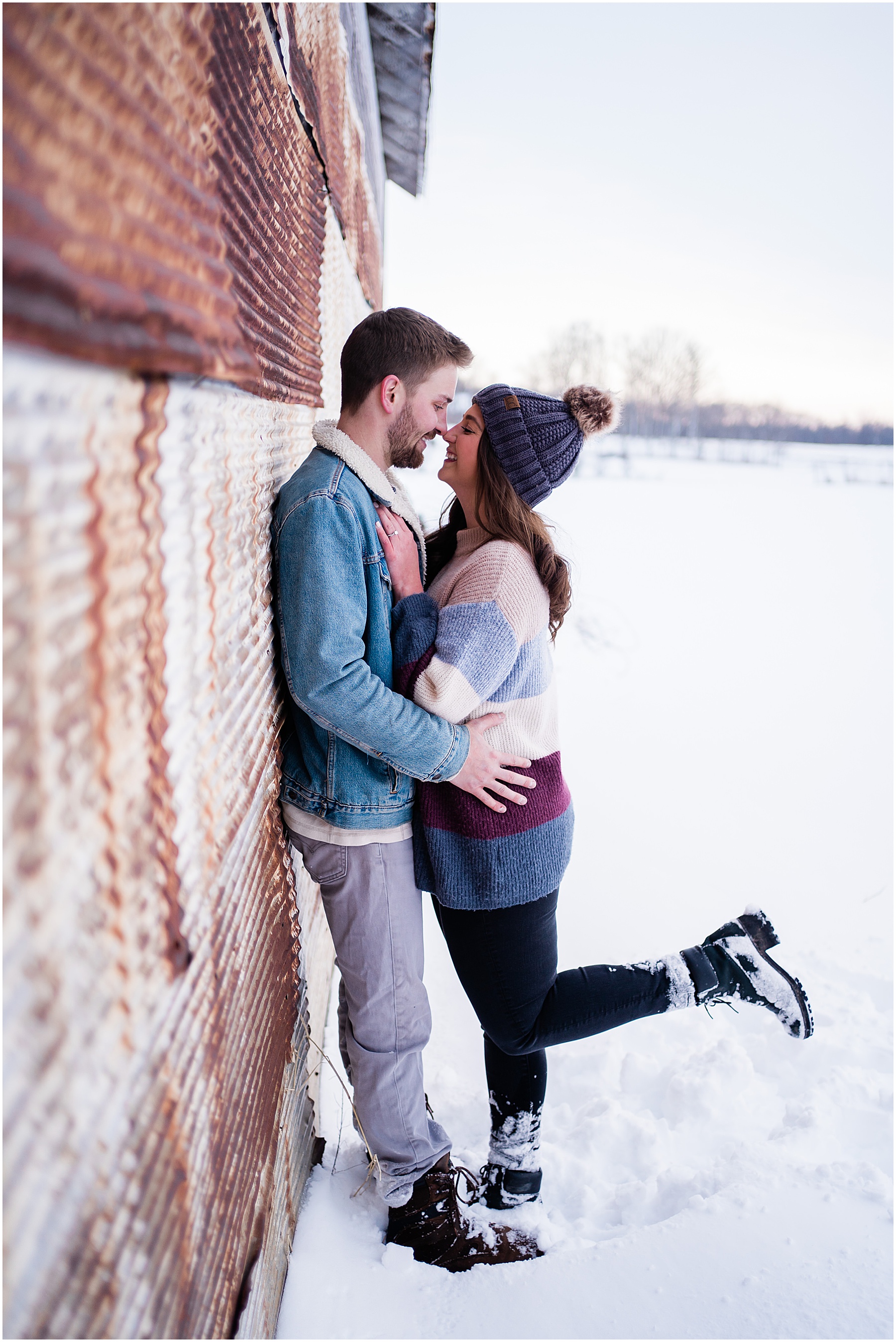 engaged couple leaning against barn