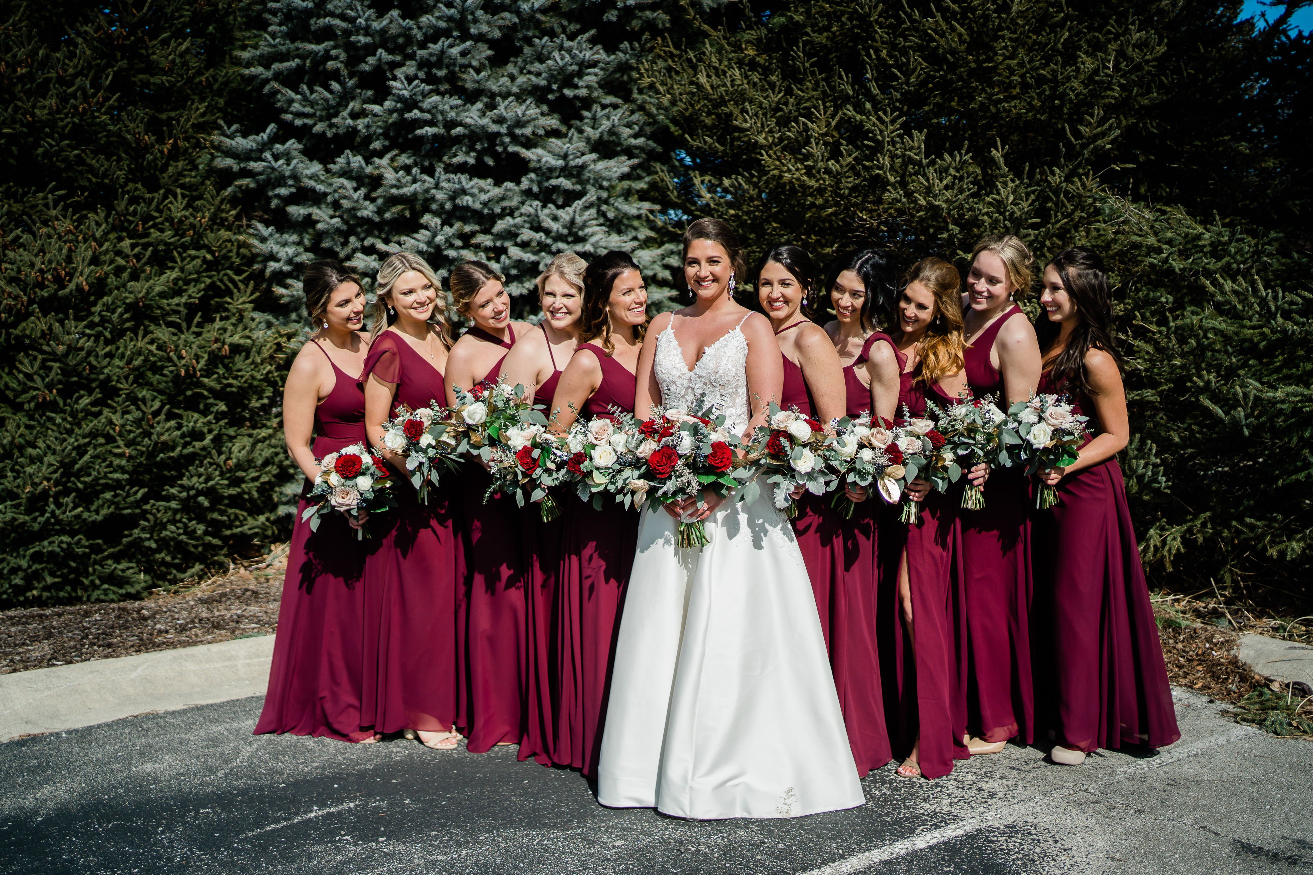 bride surrounded by her bridesmaids who are in dark red gowns holding floral bouquets