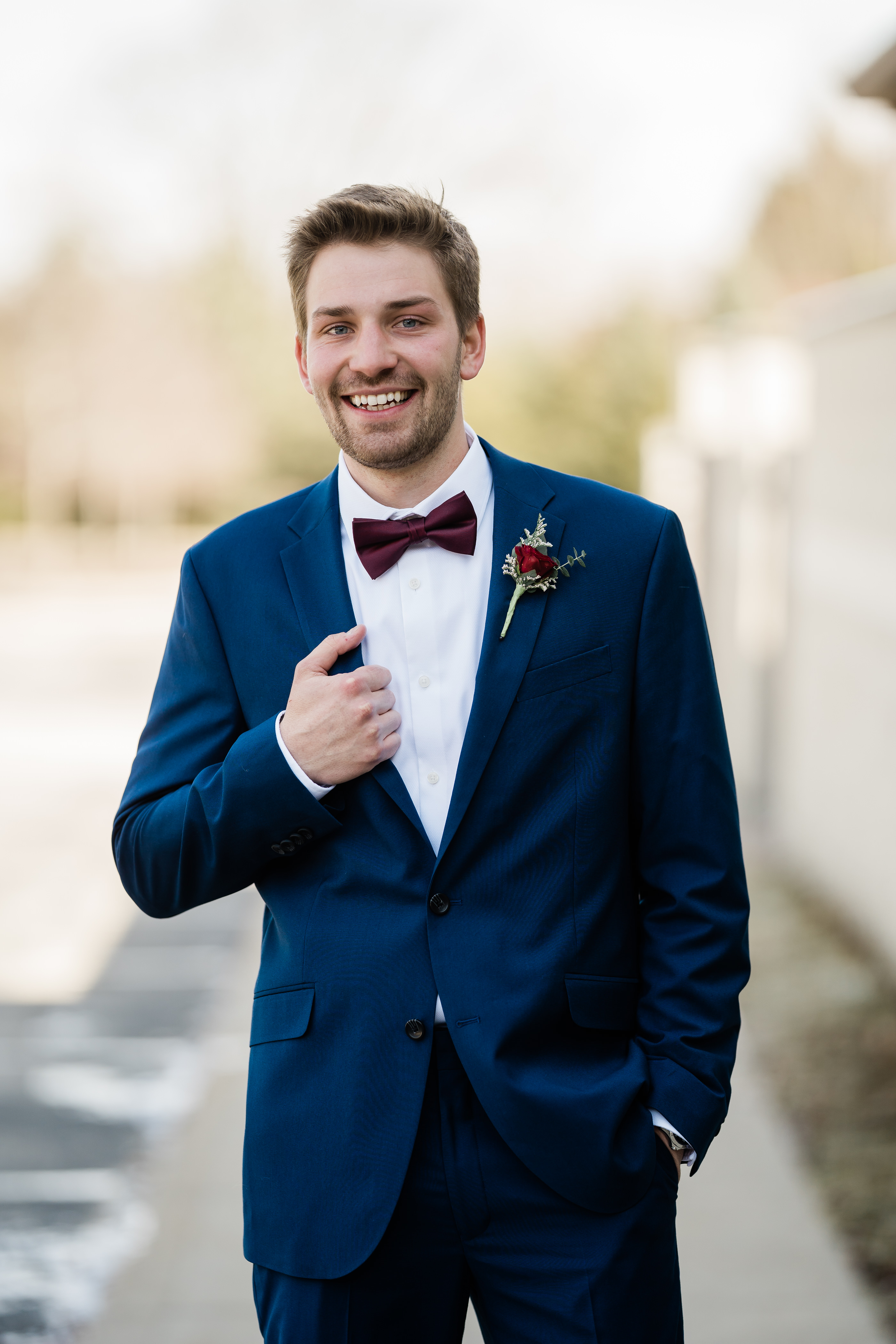 young groom with brown hair and a scruffy beard smiles and holds his suit coat