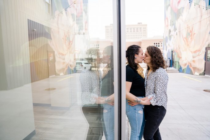 couple leaning against window kissing during engagement session
