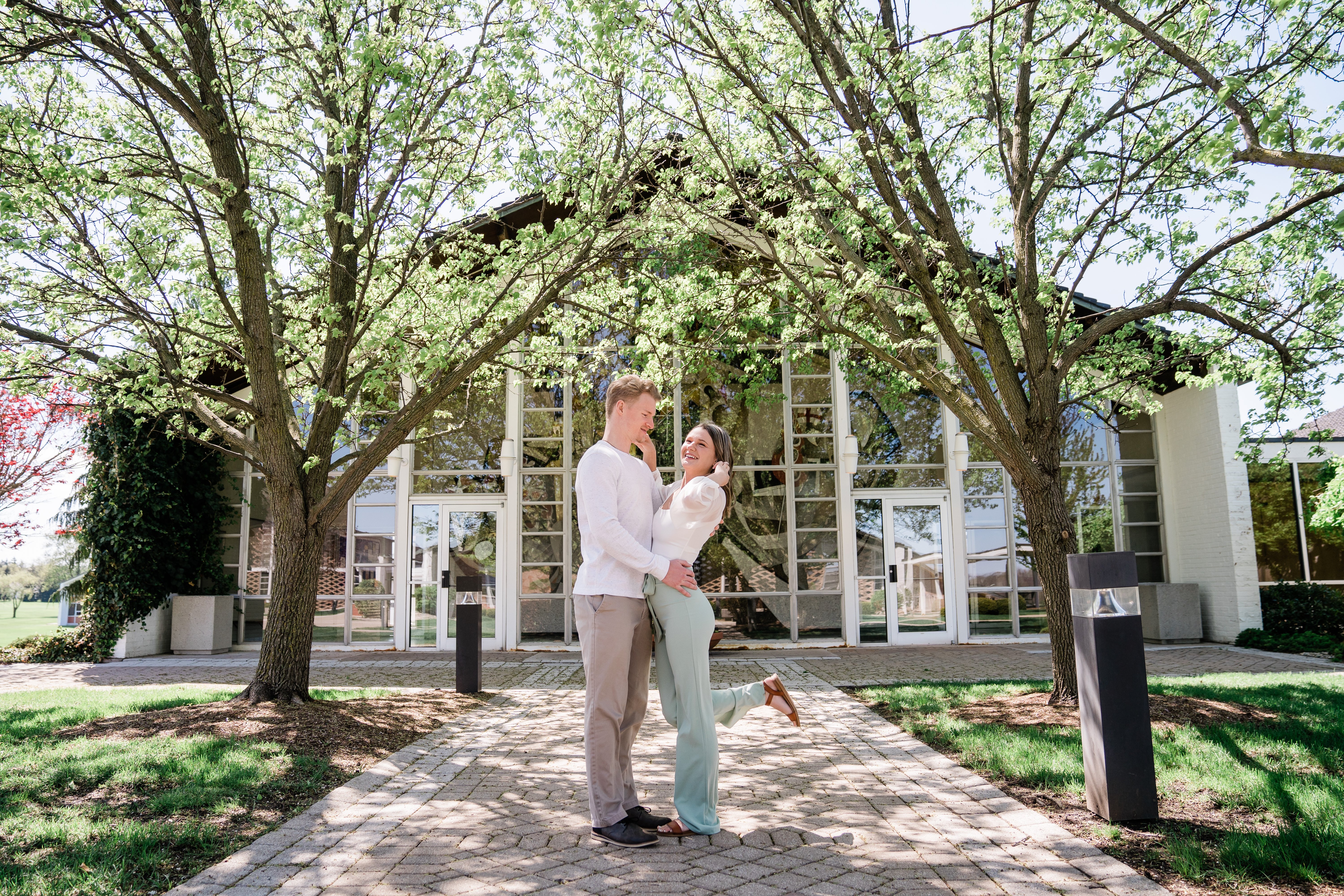 spring engagement session in Fort Wayne with man and woman in neutral colored outfits hugging each other as they stand under blossoming trees