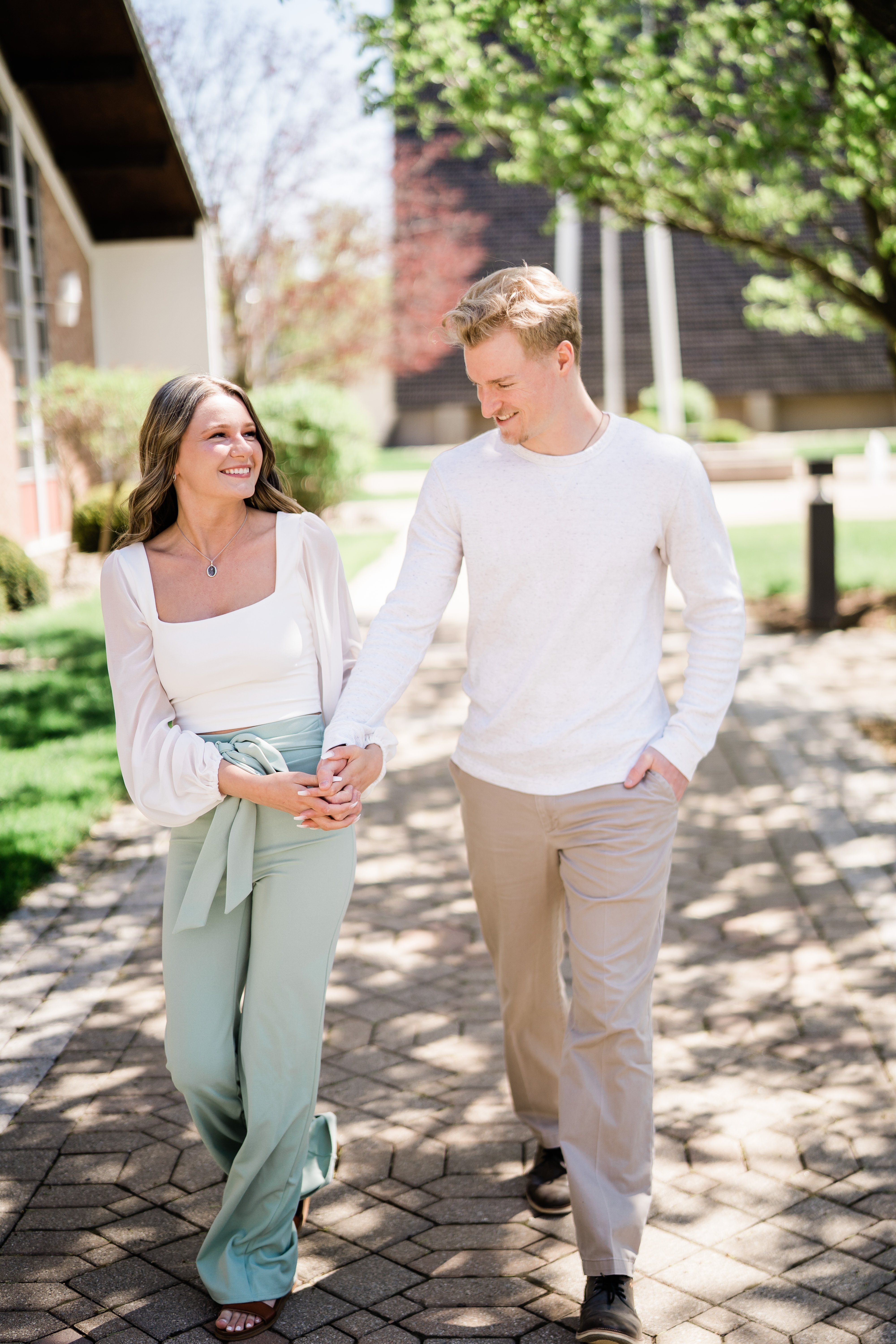 engaged couple holding hands as they walk through campus for their engagement session with Fort Wayne wedding photographer