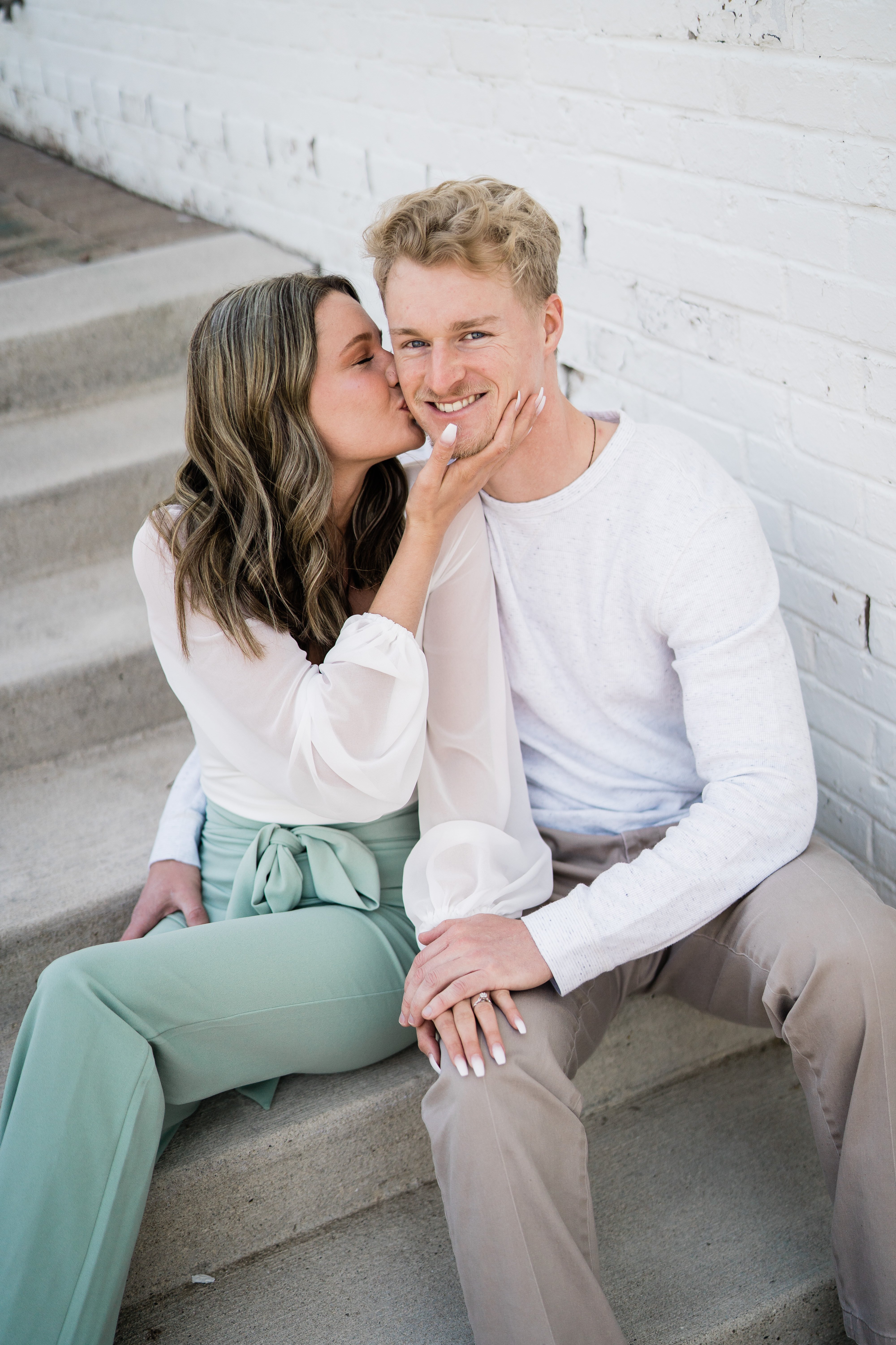 Fort Wayne engagement photos with woman and man sitting together and woman kissing the mans cheek as he smiles