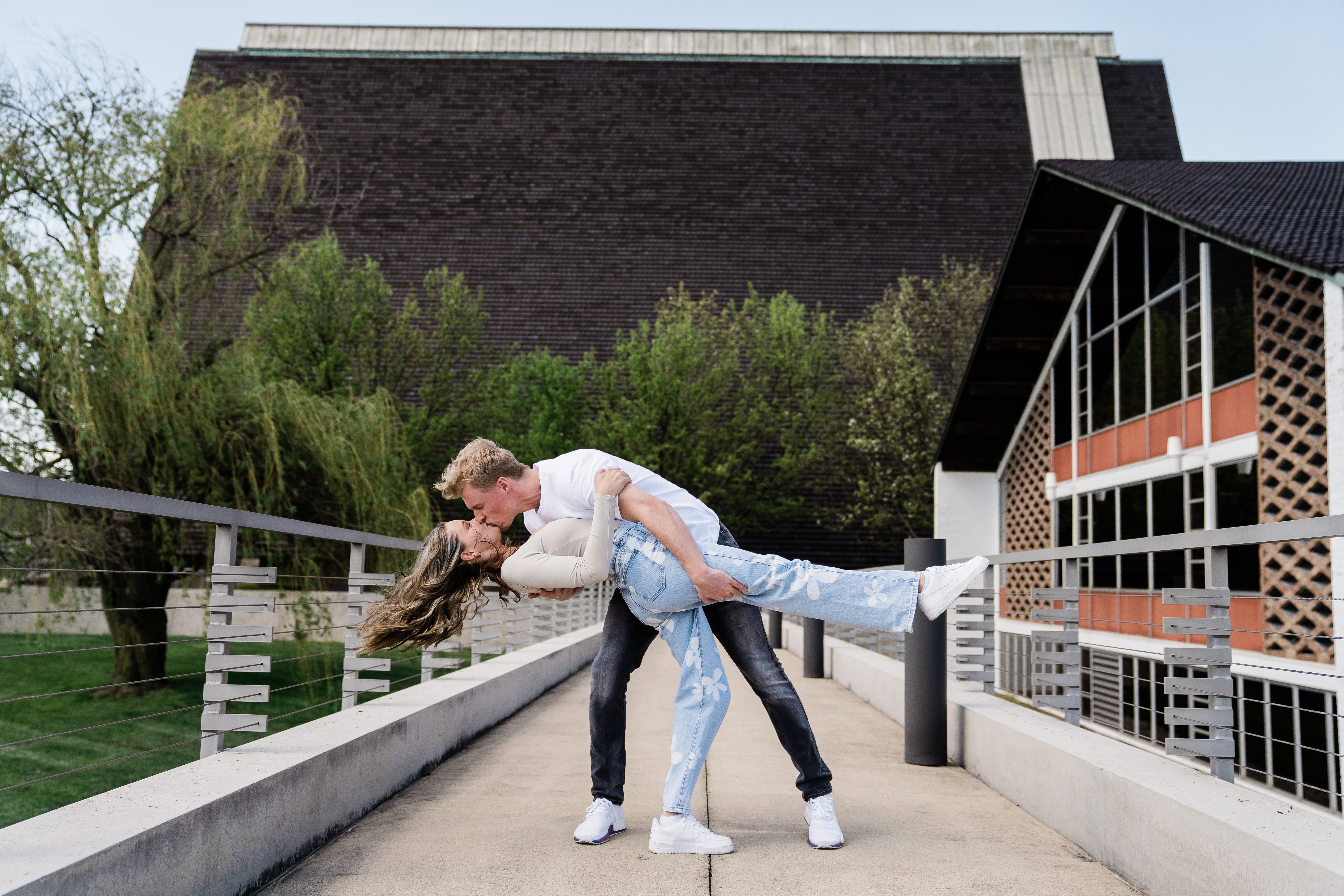 man and woman dancing on a bridge in Fort Wayne for their engagement session and man dips woman back 