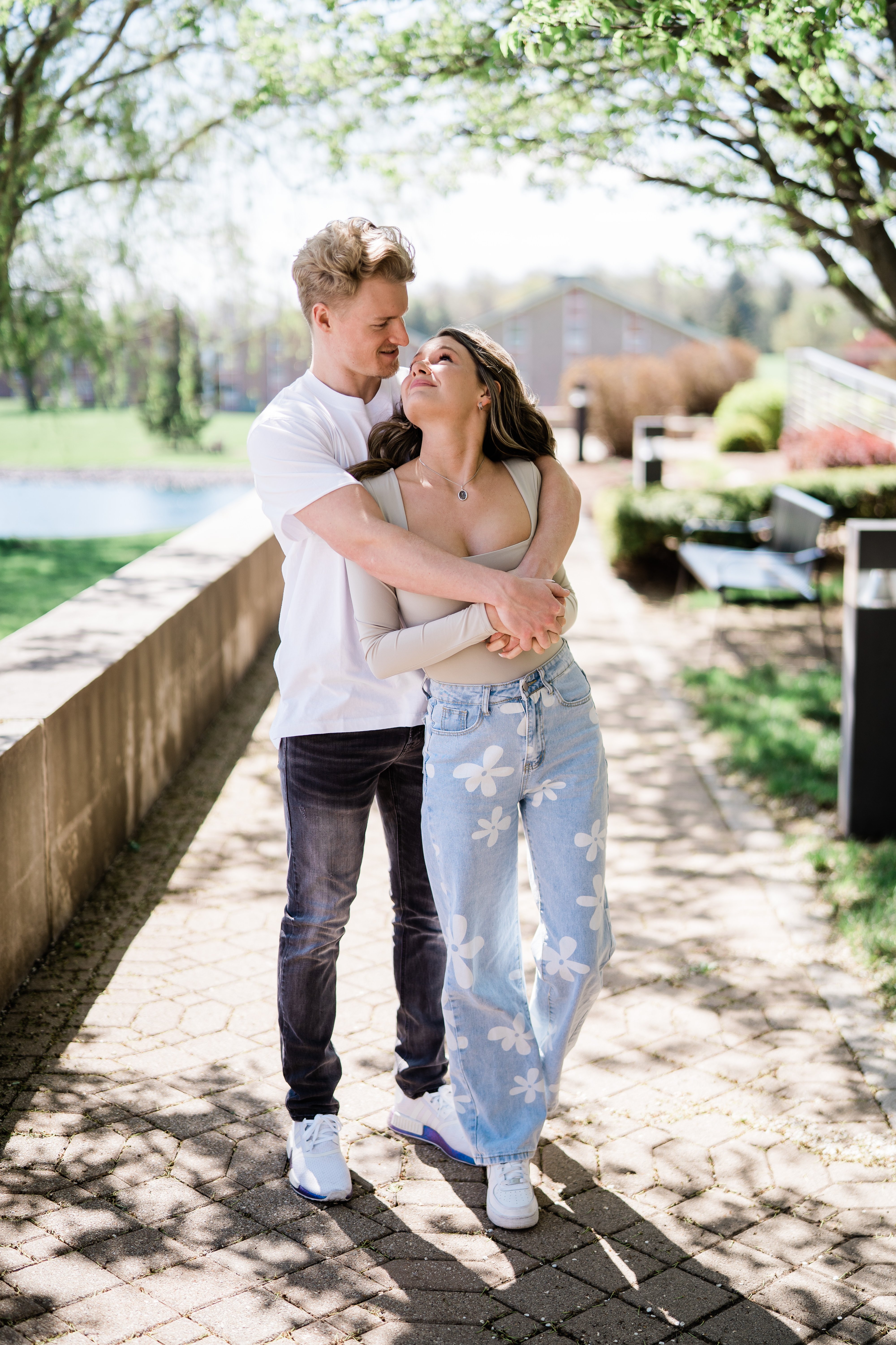 spring engagement pictures with man standing behind woman while embracing her as she looks up at him and laughs