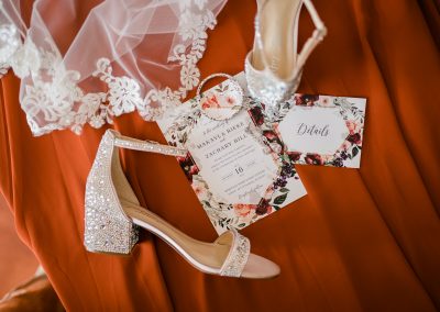 wedding veil, brides shoes and wedding invitations on top of a burnt orange fabric