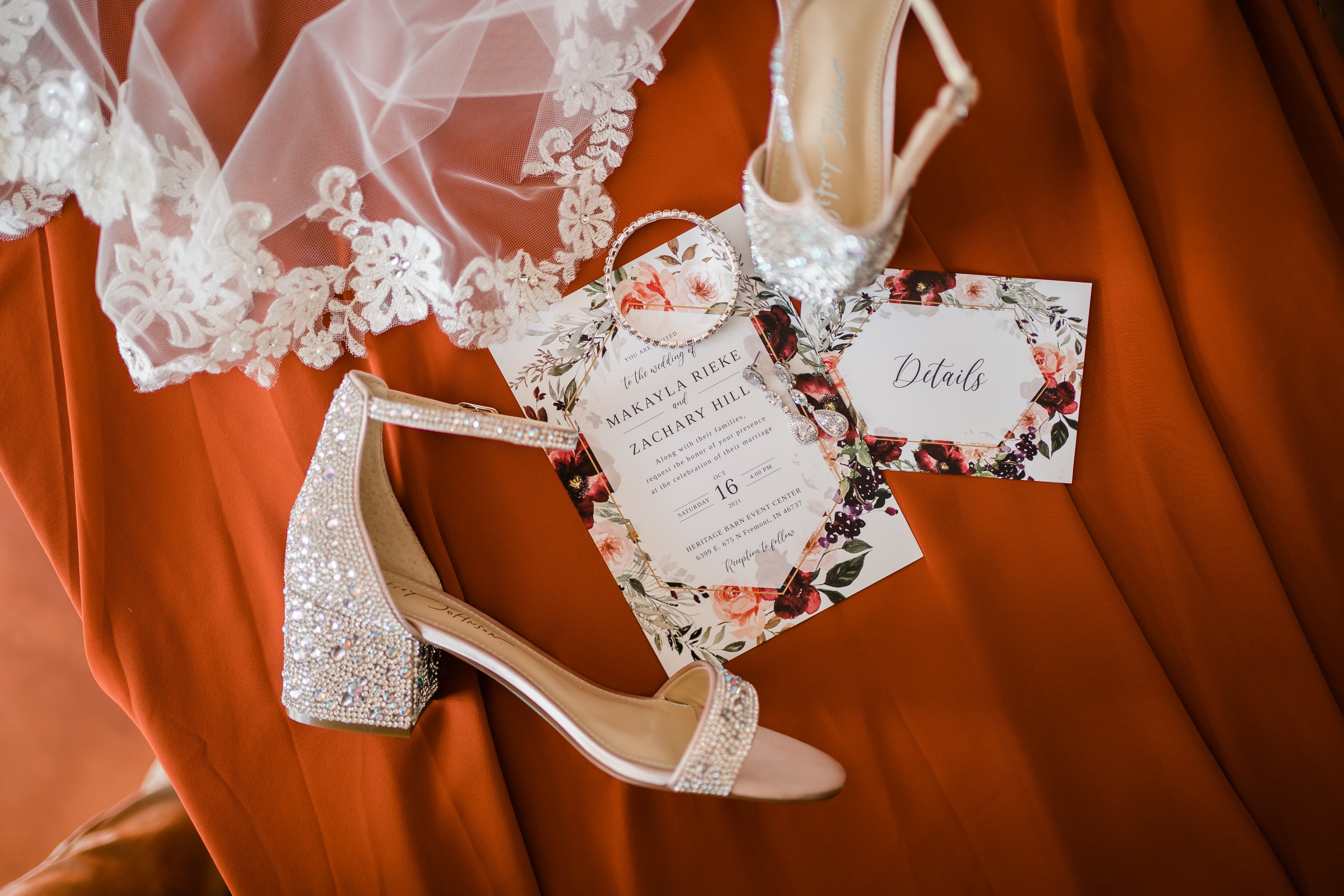wedding veil, brides shoes and wedding invitations on top of a burnt orange fabric