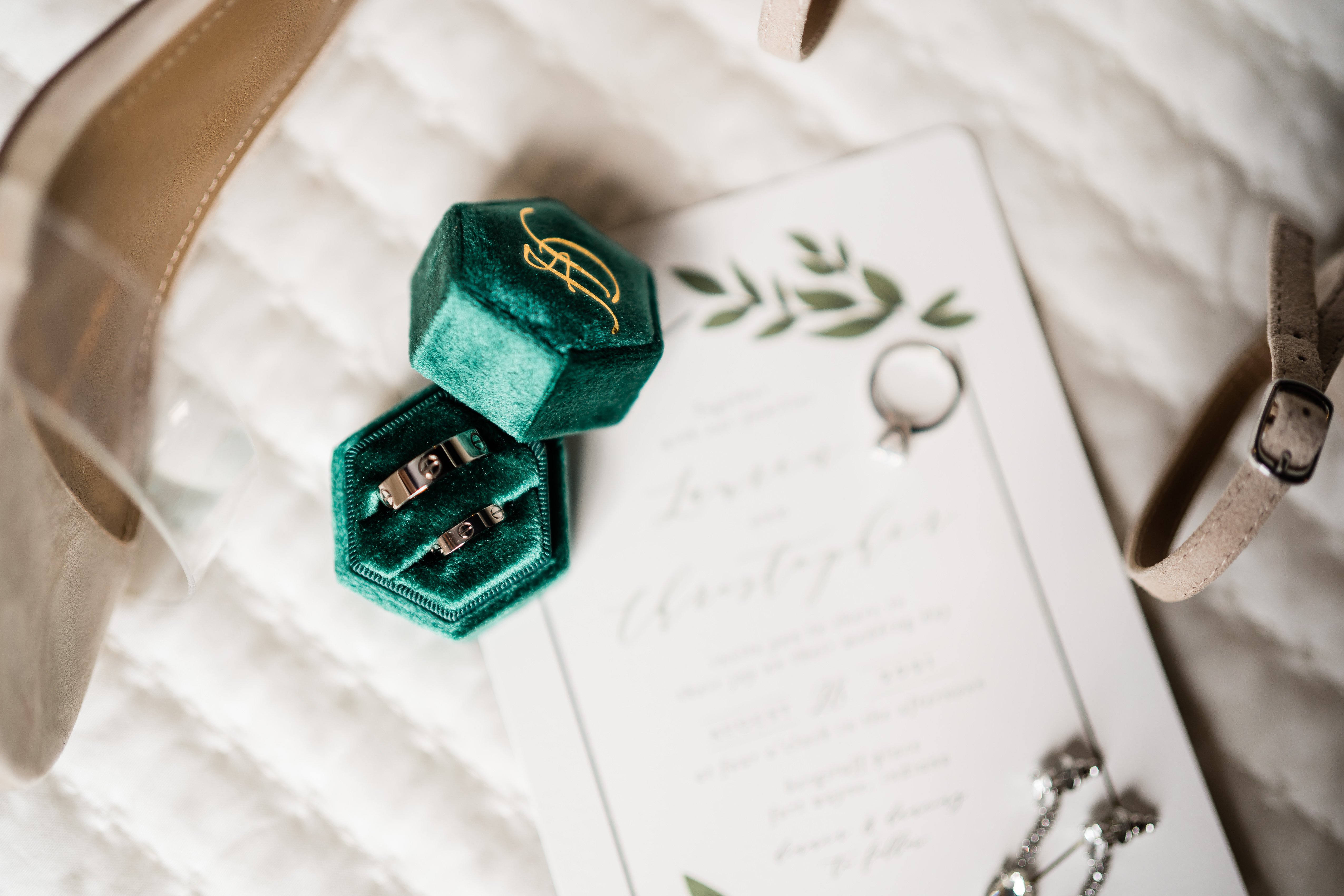 wedding ring in a green velvet box with an invitation to the wedding behind it