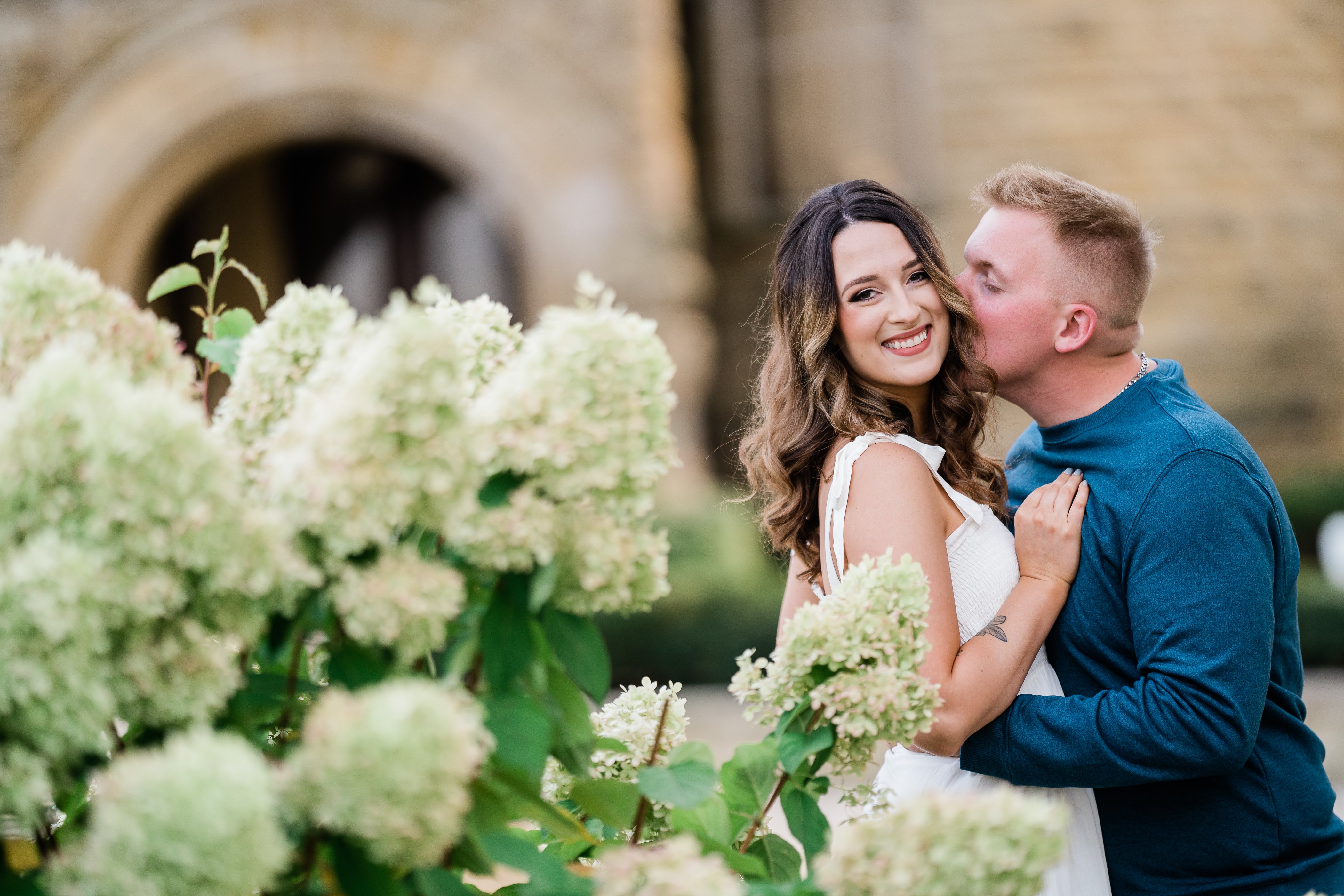 engagement photos with man and womanin a white dress posing next to a bush of hydrangeas in Fort Wayne 