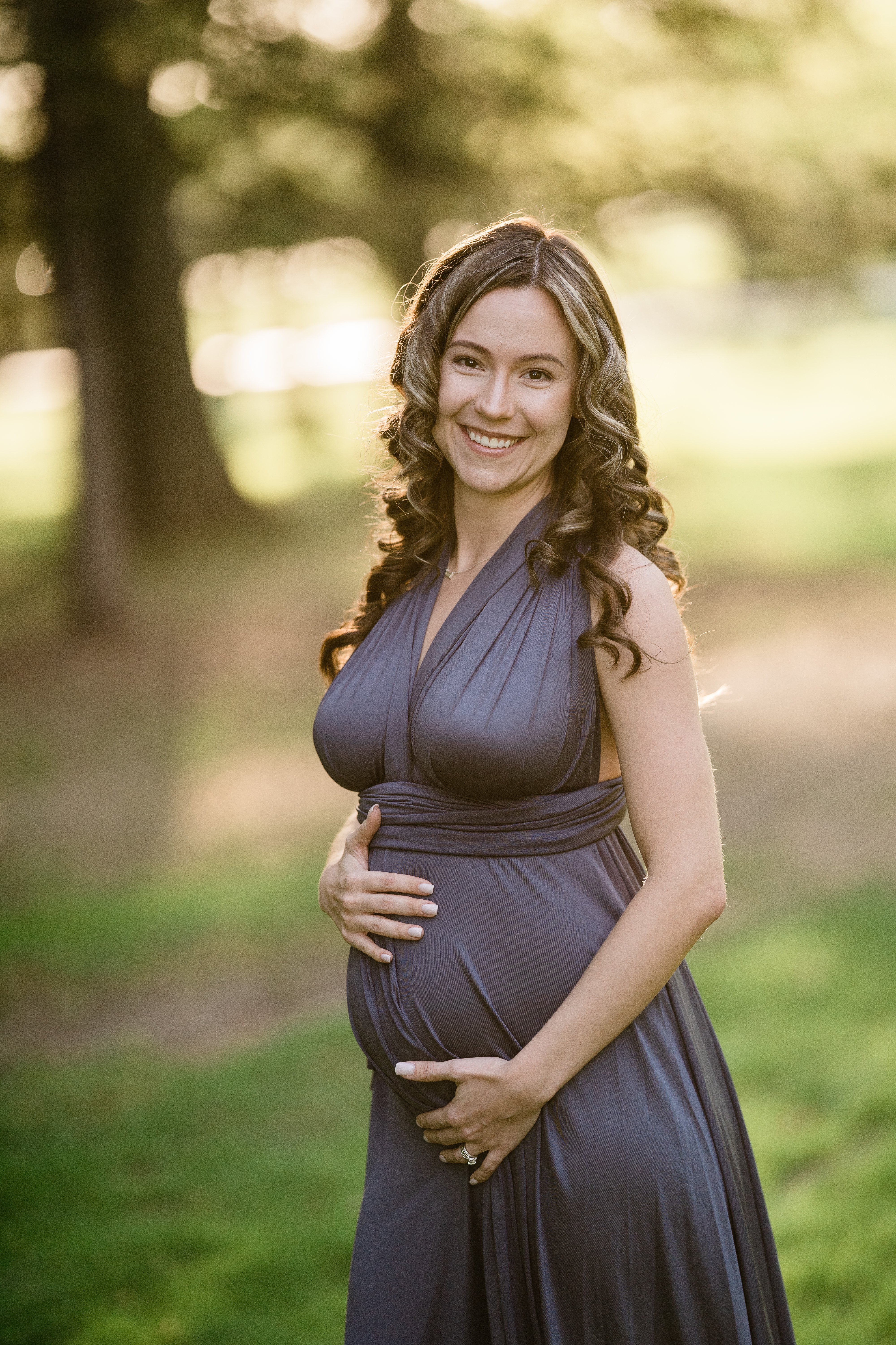 expecting mother in a blue maternity dress in a forest holding her bump for Fort Wayne maternity session