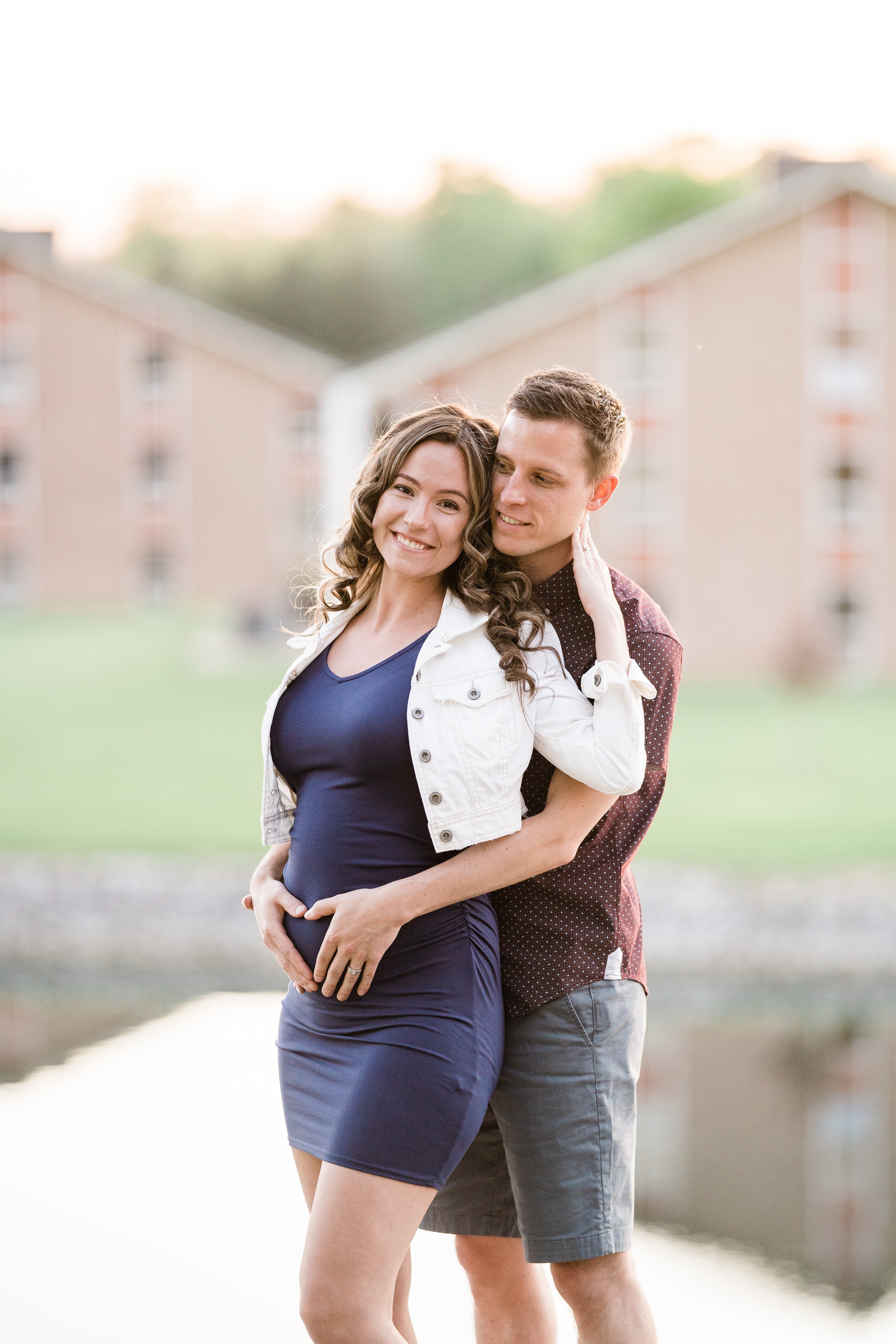 wife holds her husbands neck as he embraces her baby bump for their maternity photos