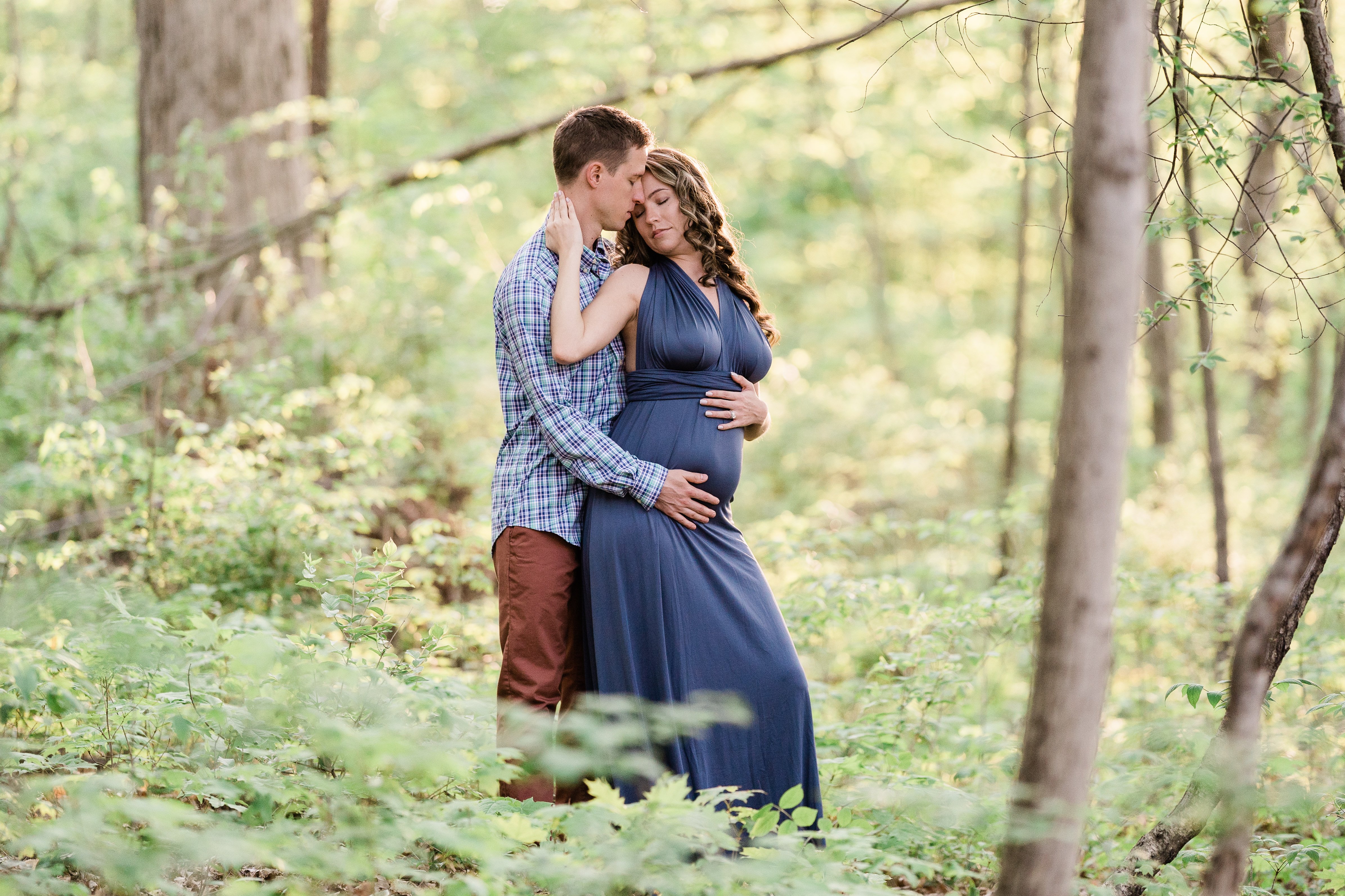 man and pregnant wife embrace in the woods for their Fort Wayne maternity session 