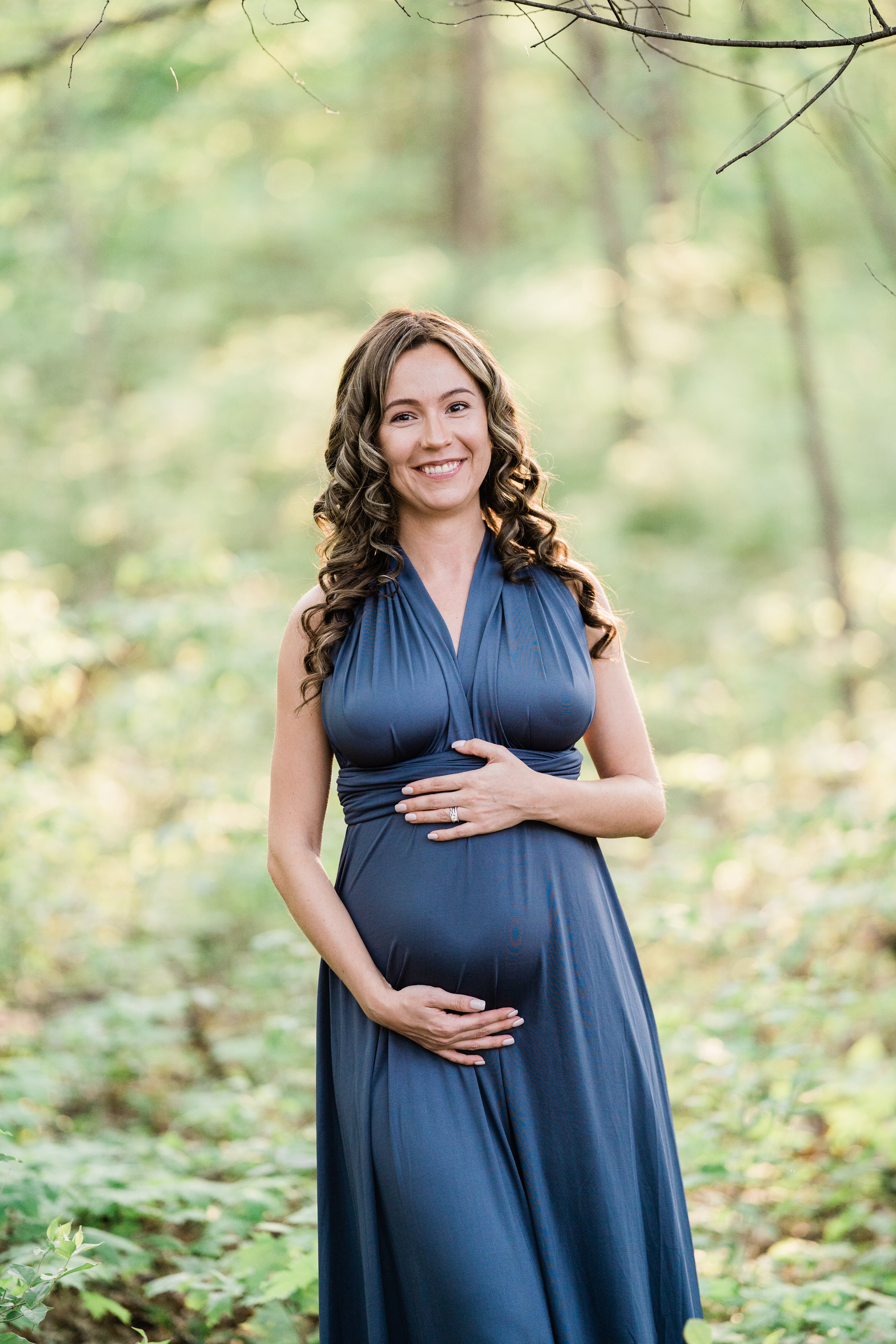 pregnant woman in a blue dress in the woods holding her pregnancy bump