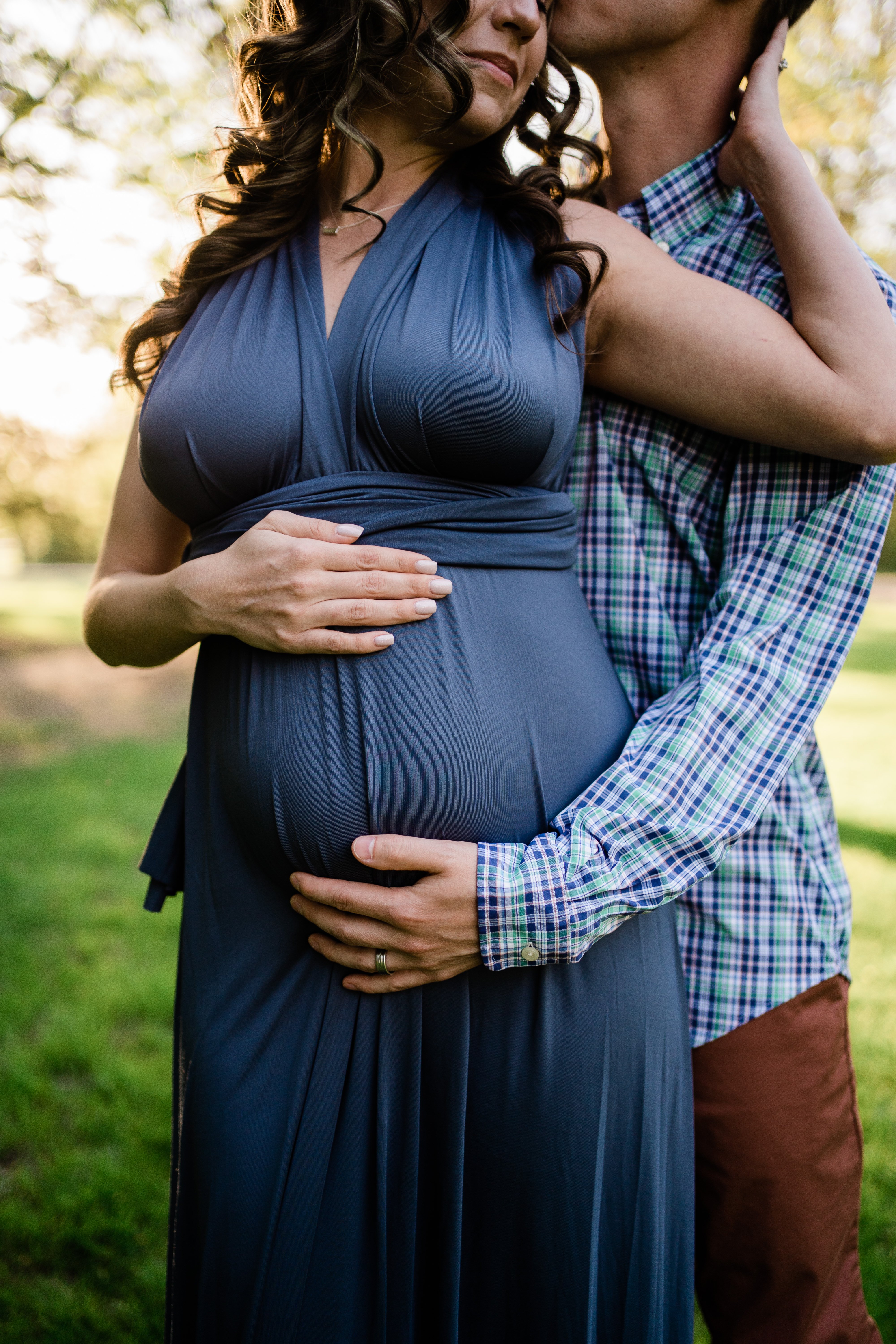 husband standing behind his wife and holding her baby bump as she reach back to caress his face