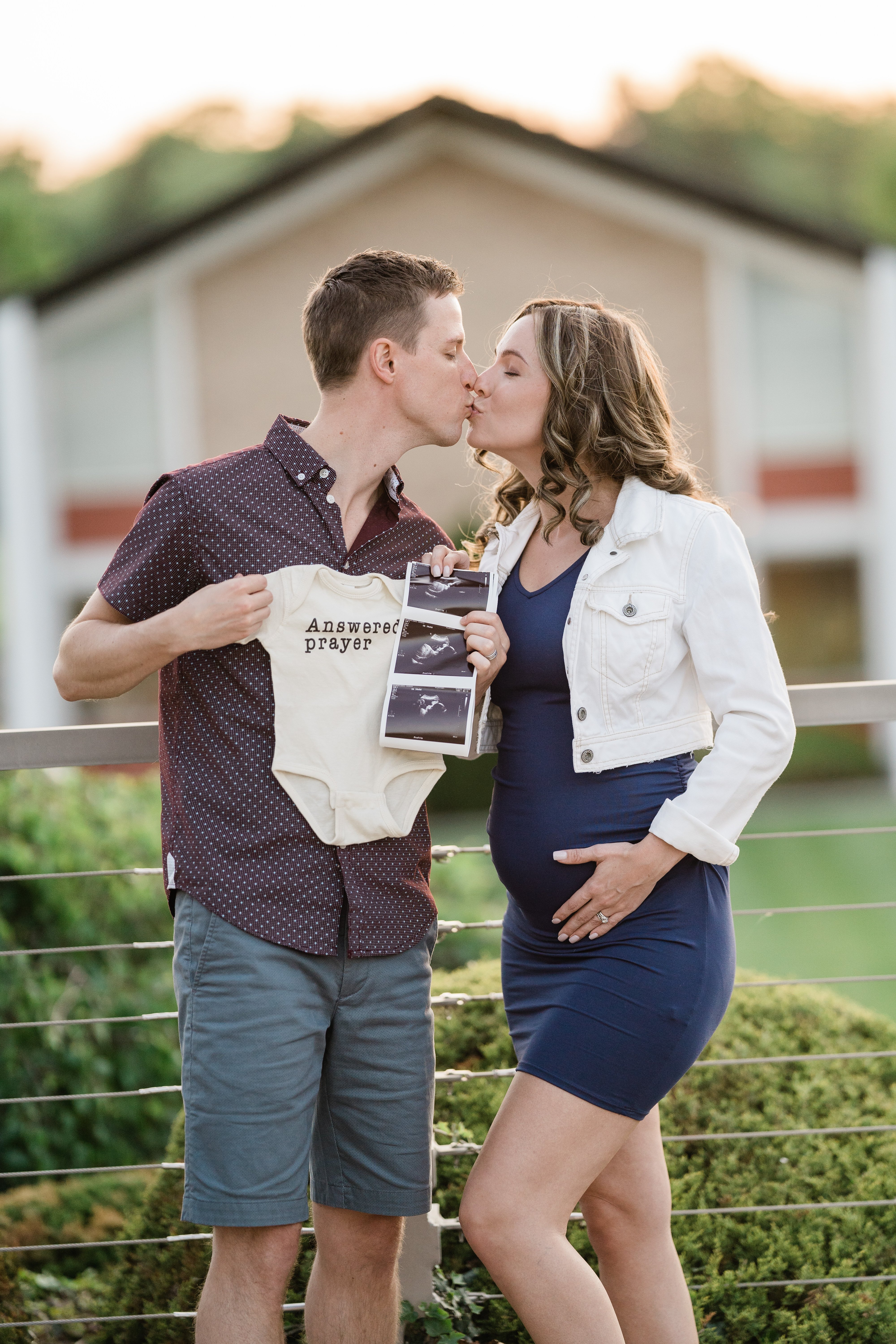 husband and wife kissing during their maternity session with onesie and ultrasound