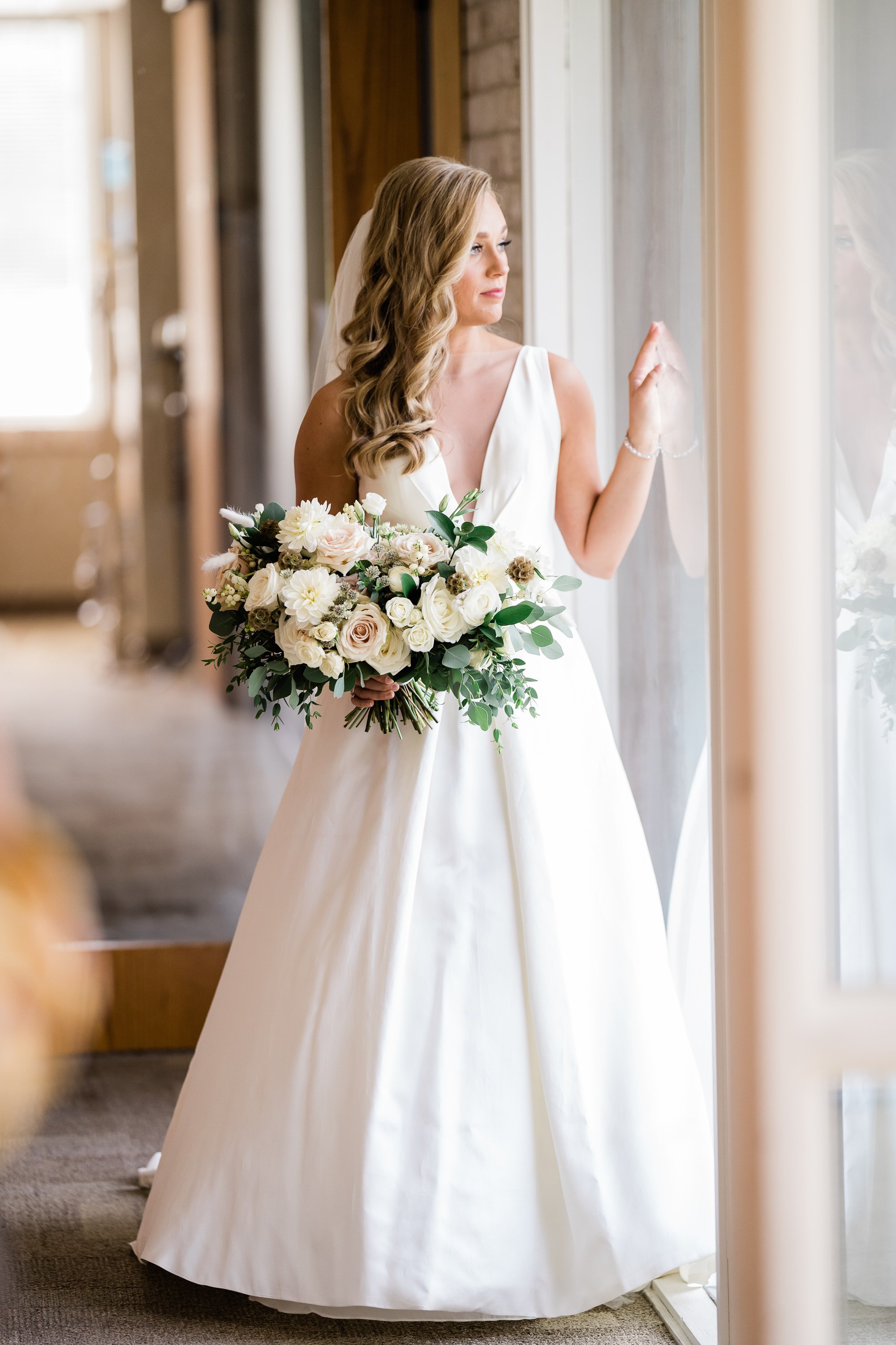Fort Wayne bride in a satin wedding gown holding a white floral bouquet looks over a balcony for her bridal portraits taken by Fort Wayne wedding photographers
