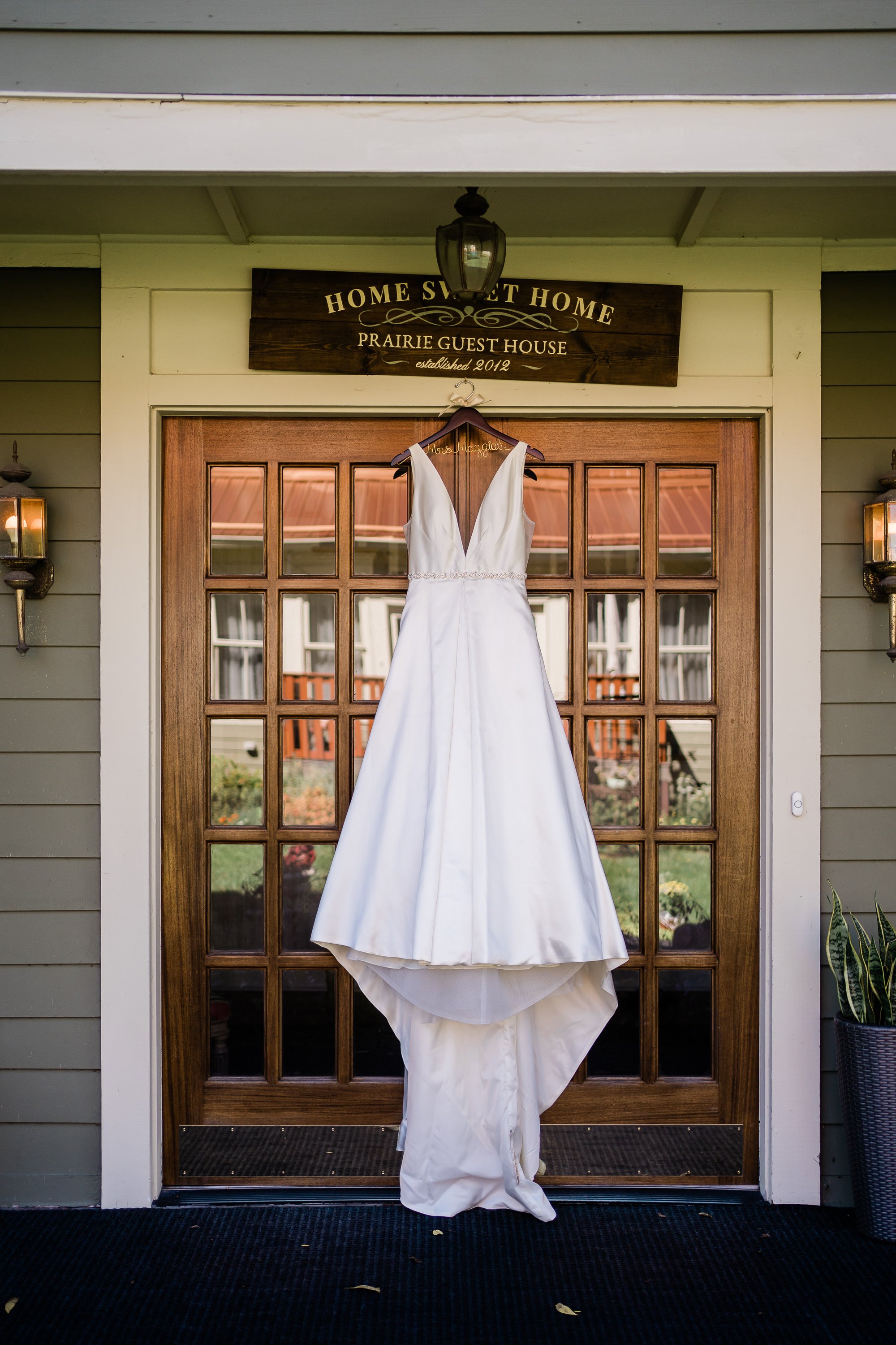wedding dress hanging from a wooden hanger while hanging over a front door that are french doors on a front porch