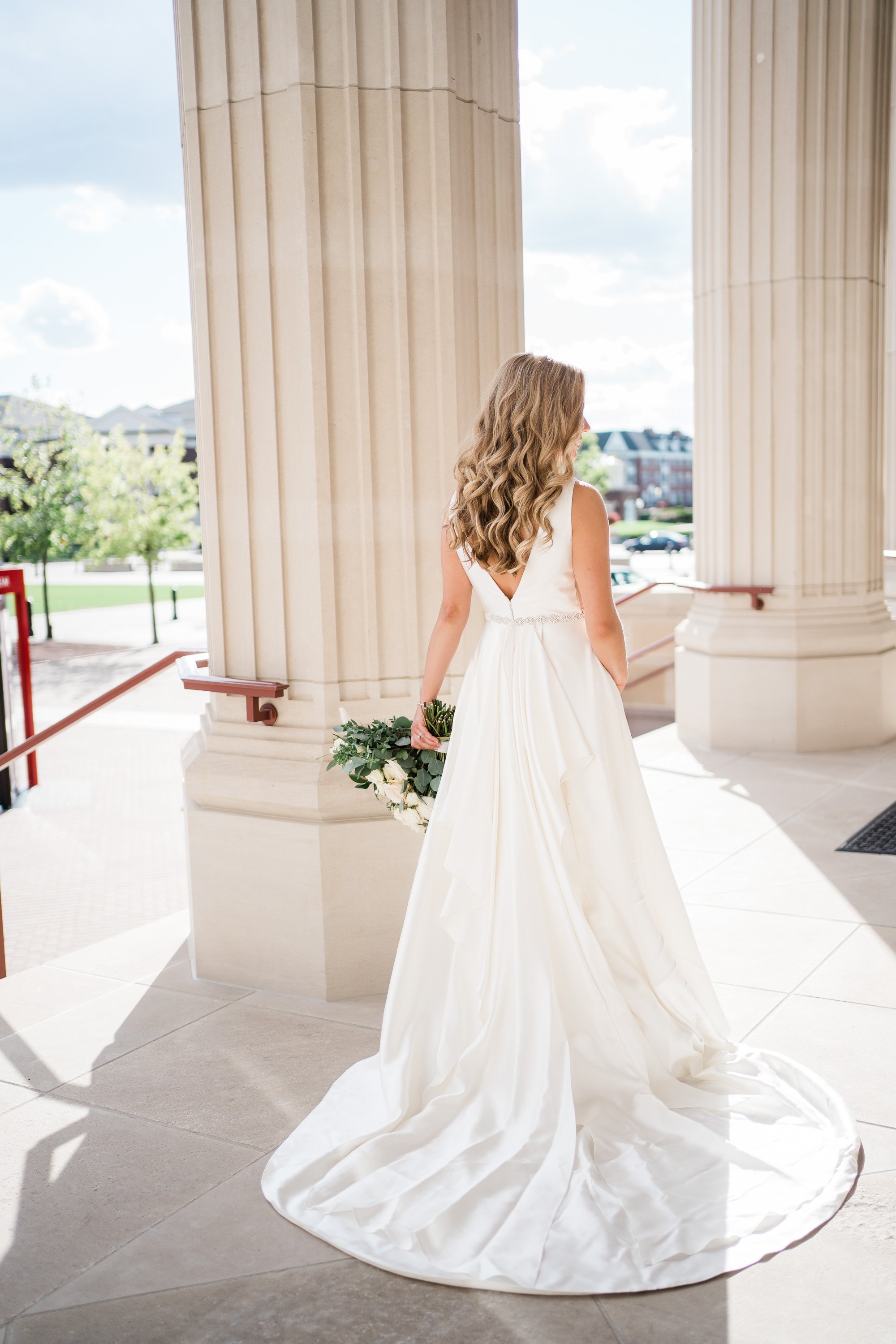 bride walking through pillars of their luxury wedding venue with her train behind her