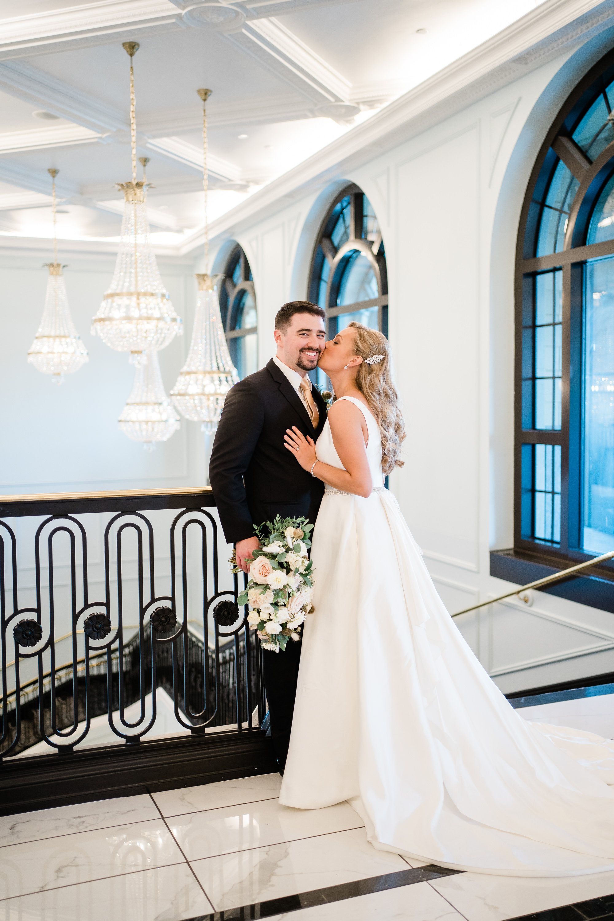 bride kissing her groom on the cheek as he smiles at the camera inside of their Fort Wayne wedding venue captured by Fort Wayne wedding photographers