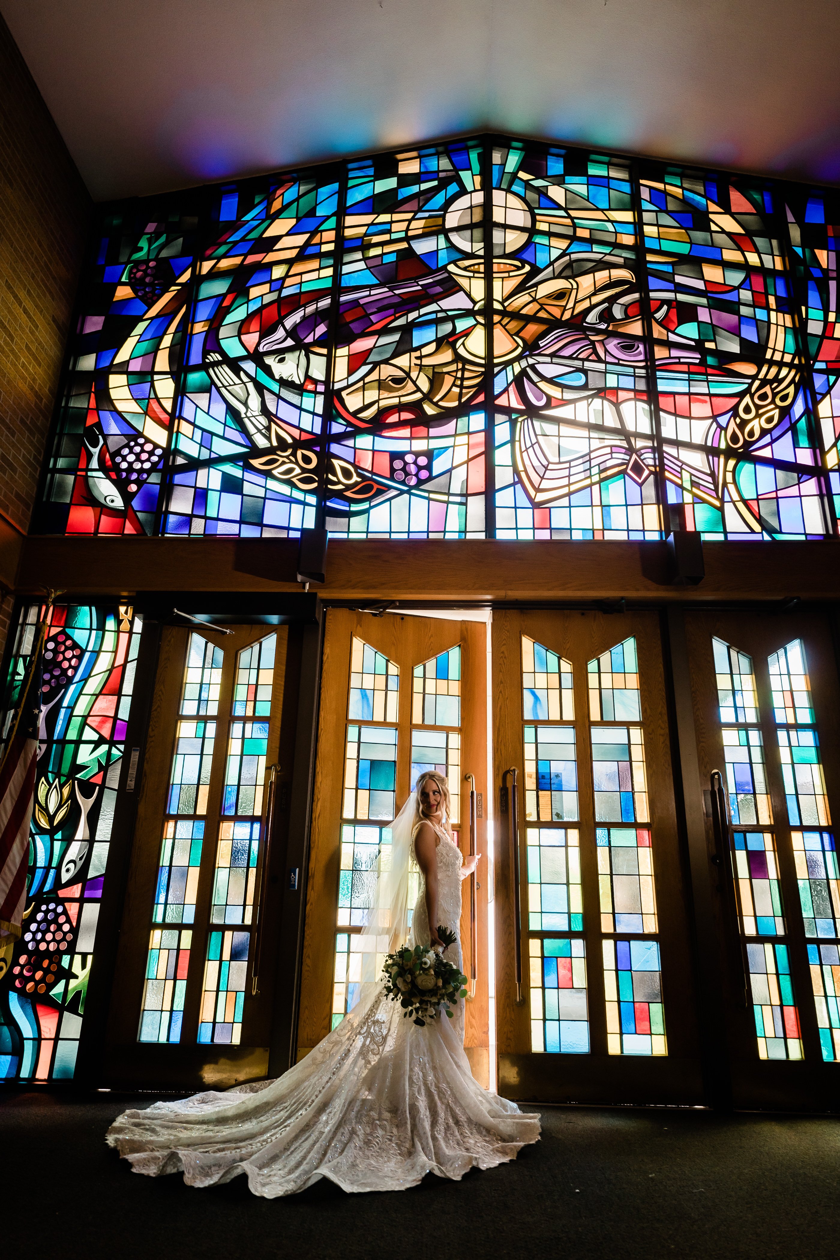 bride in a lace wedding dress standing in front of the stain glass for her church for her Fort Wayne wedding