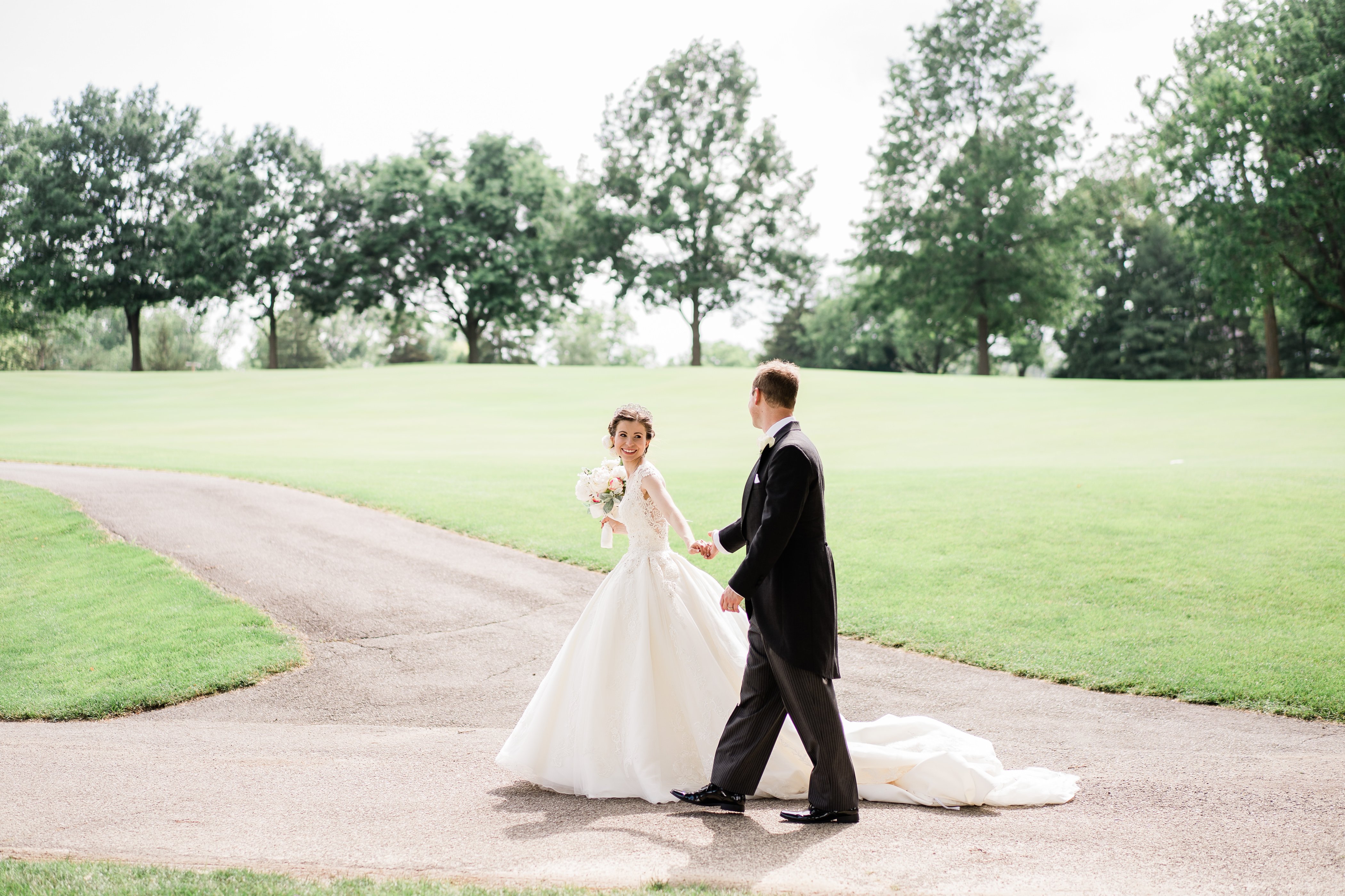 summer outdoor wedding with bride and groom holding hands and walking along a dirt path together on a golf course wedding venue 