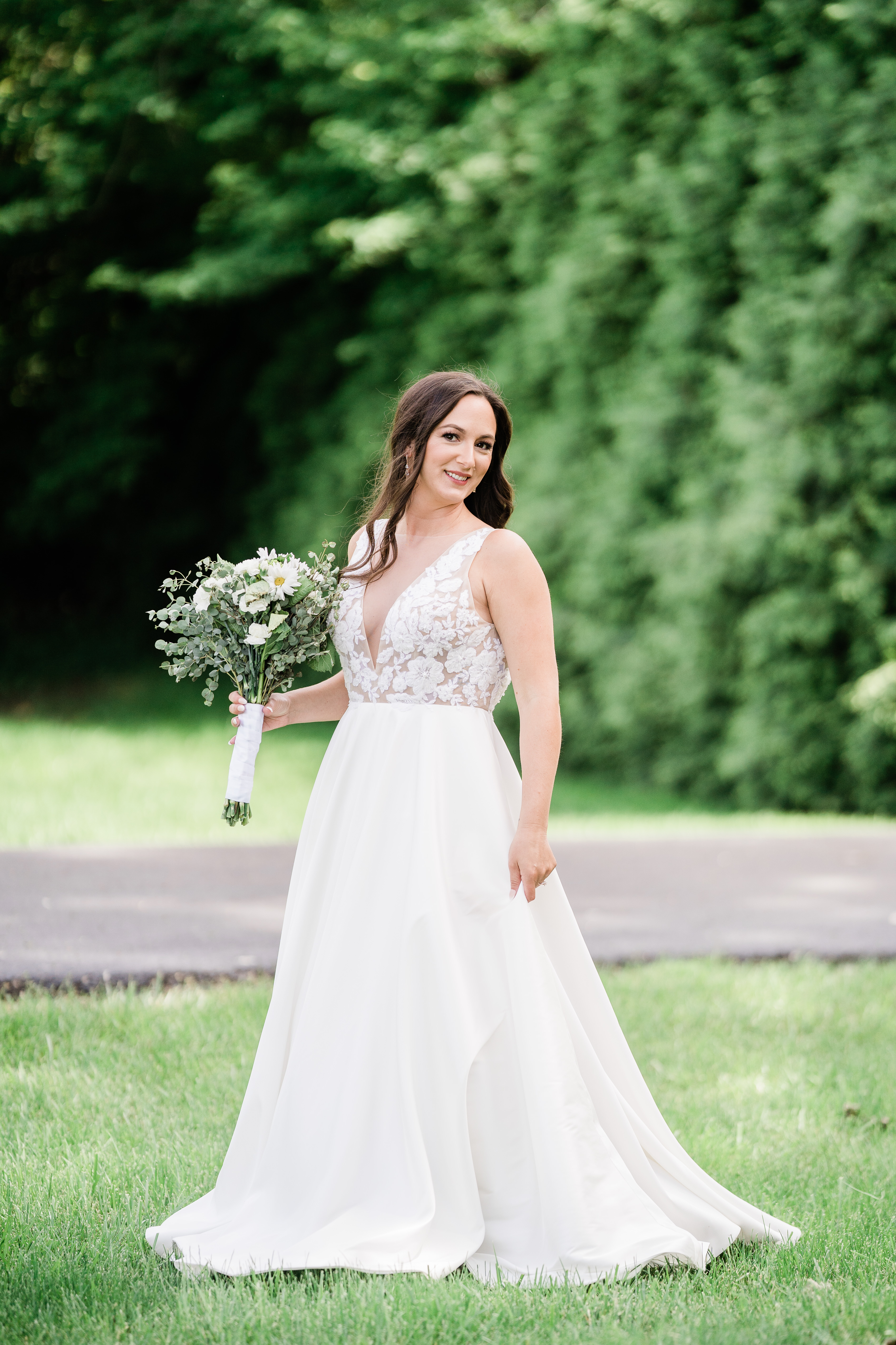 bridal picture with bride in a low v neck wedding dress walking through a lawn while holding her white wedding bouquet