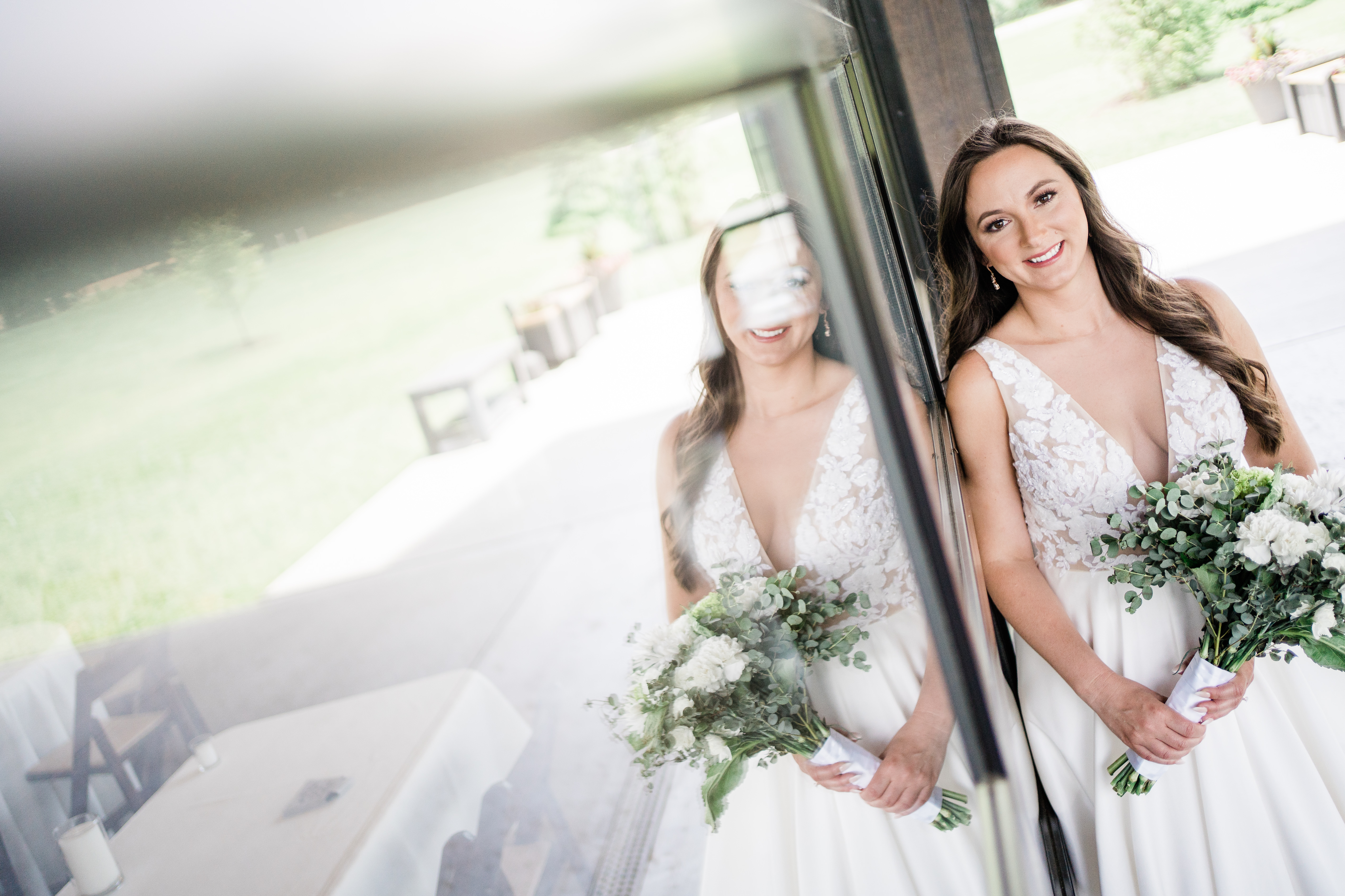 bride leaning against a glass garage door at her outdoor wedding venue