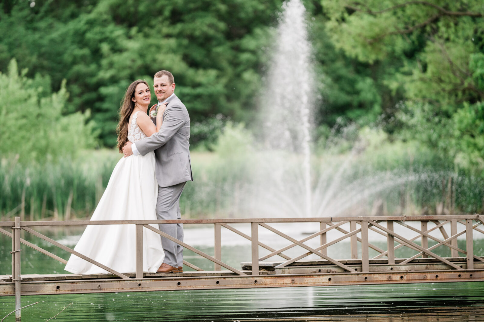 bride and groom embracing on a bridge together with a water feature behind them 