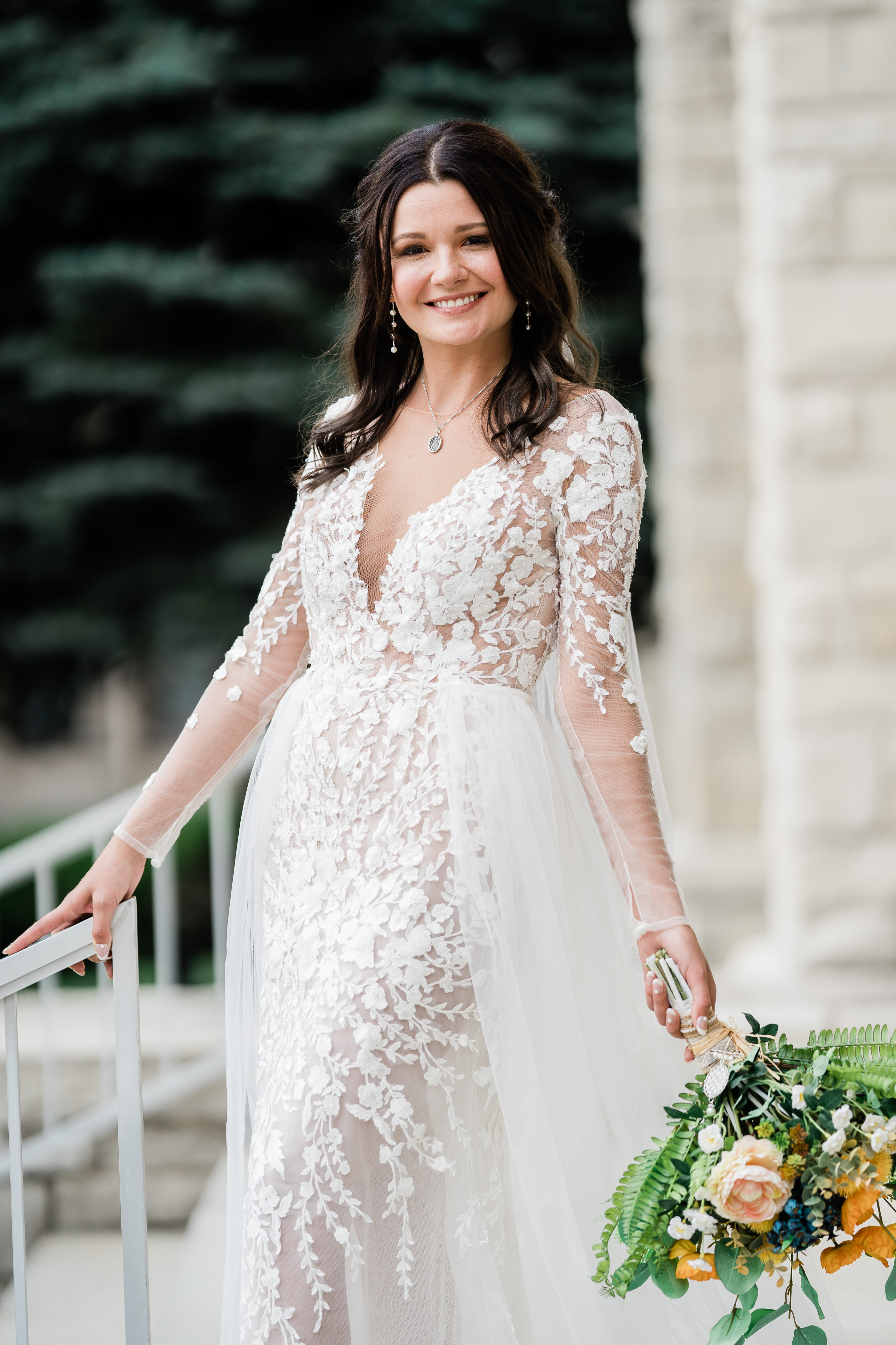 bride in a long sleeve lace wedding dress standing on a chapel's stairs outside of her wedding venue in Fort Wayne