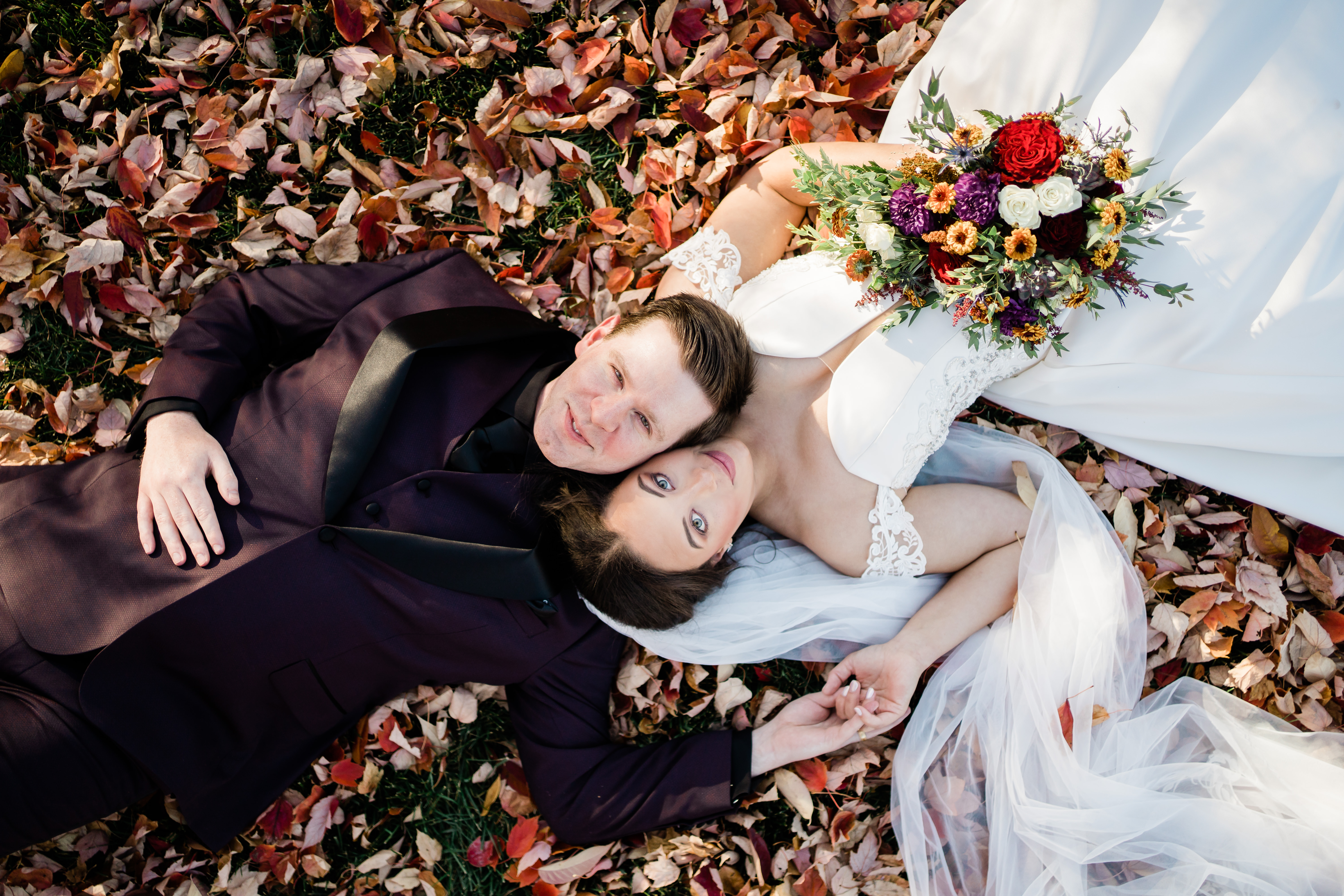 bride and groom laying in leaves on ground before wedding reception
