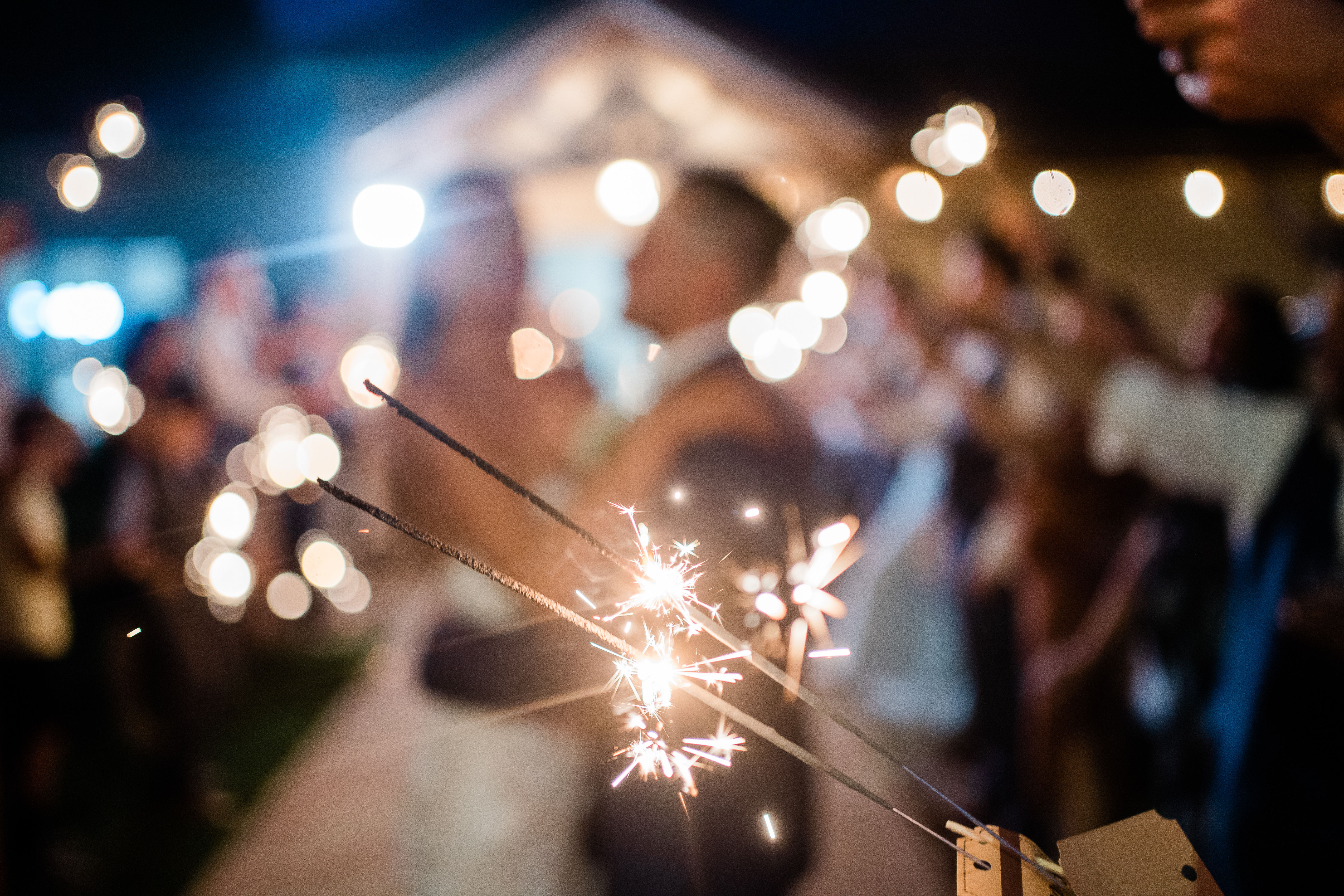 Fort Wayne wedding photographers capture close up of sparklers with couple in the background leaving wedding