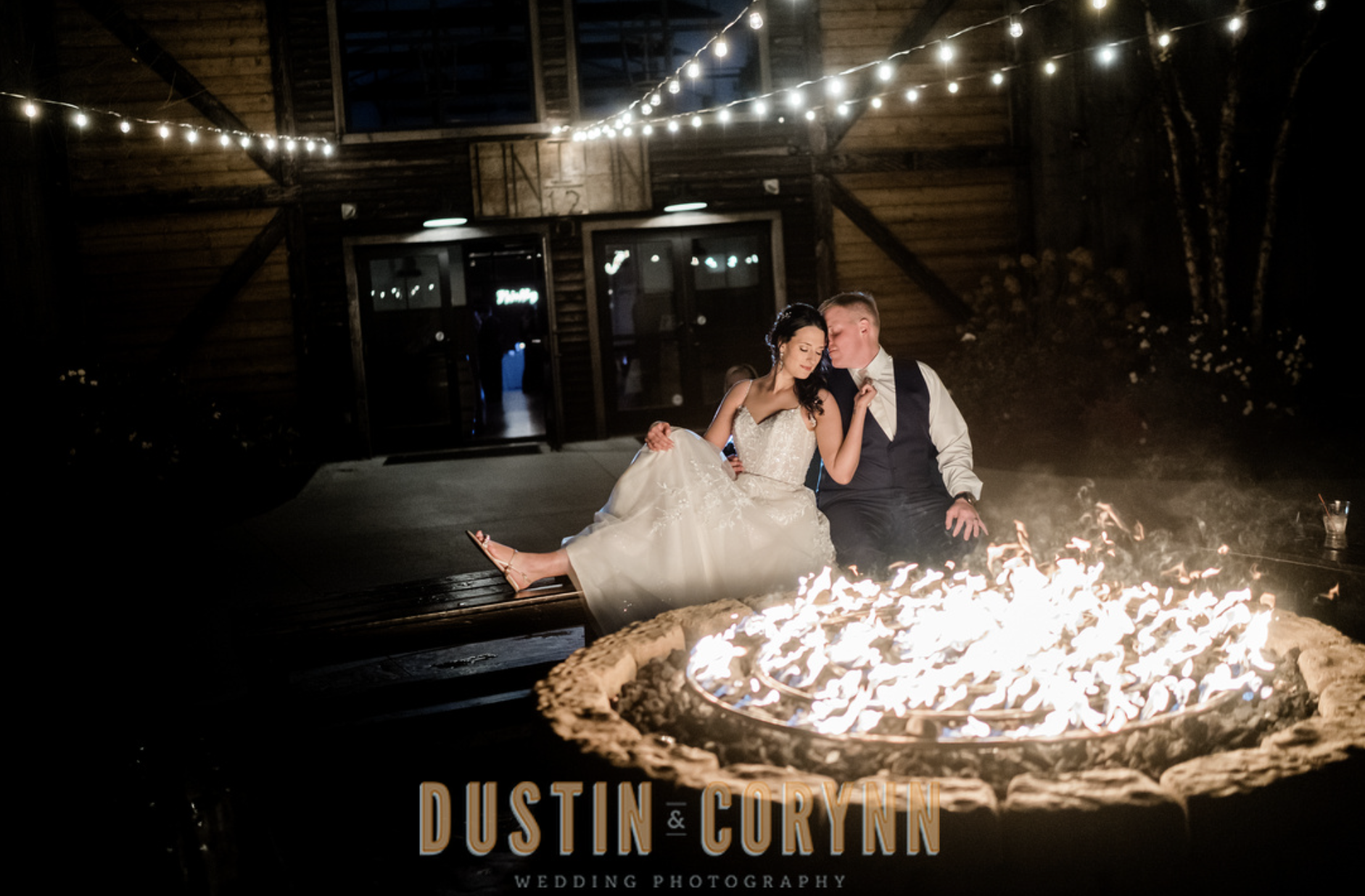 bride and groom sit together in front of fire pit celebrating